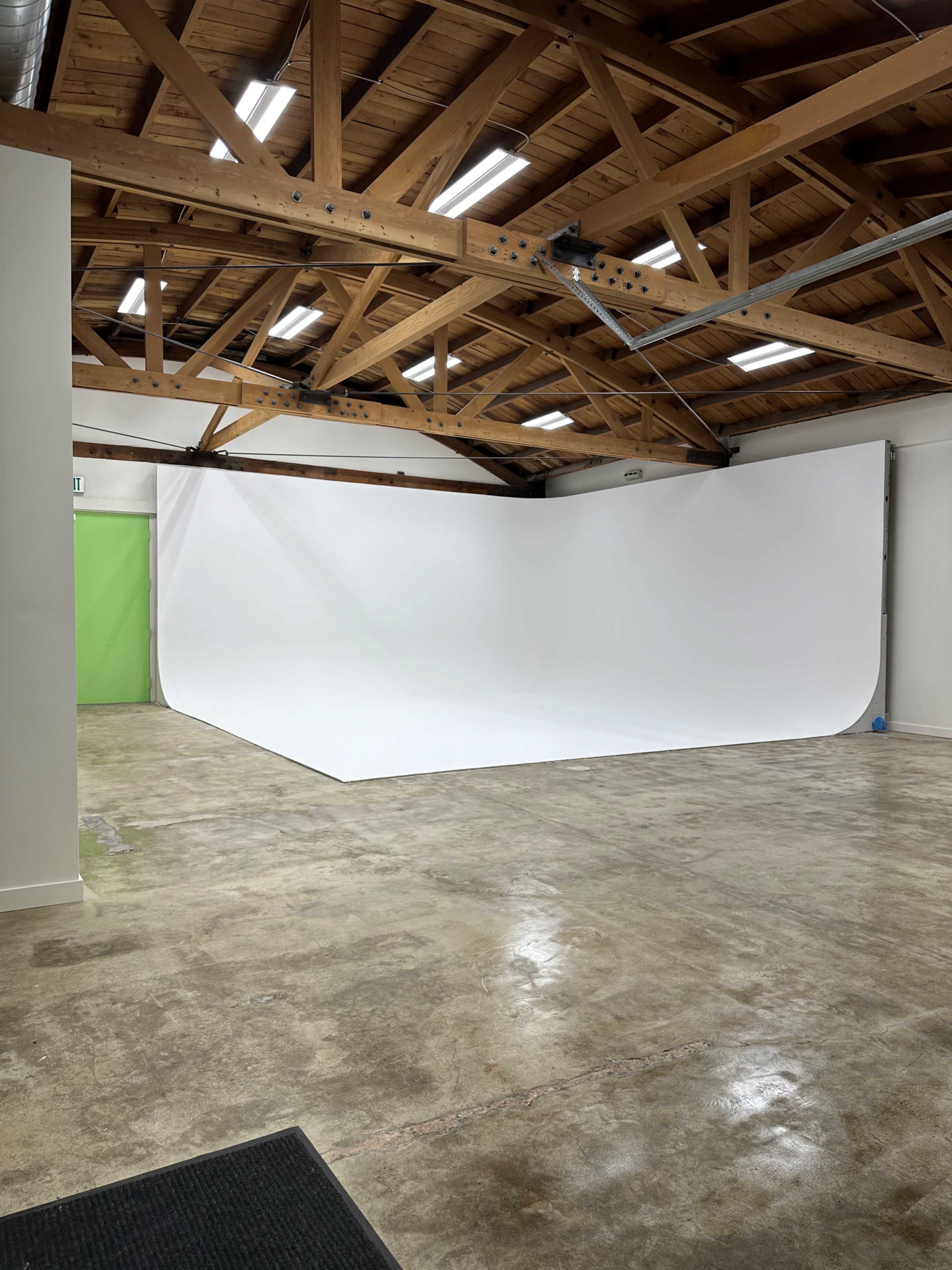 A spacious photo studio with a white backdrop and exposed wooden beams in the ceiling.
