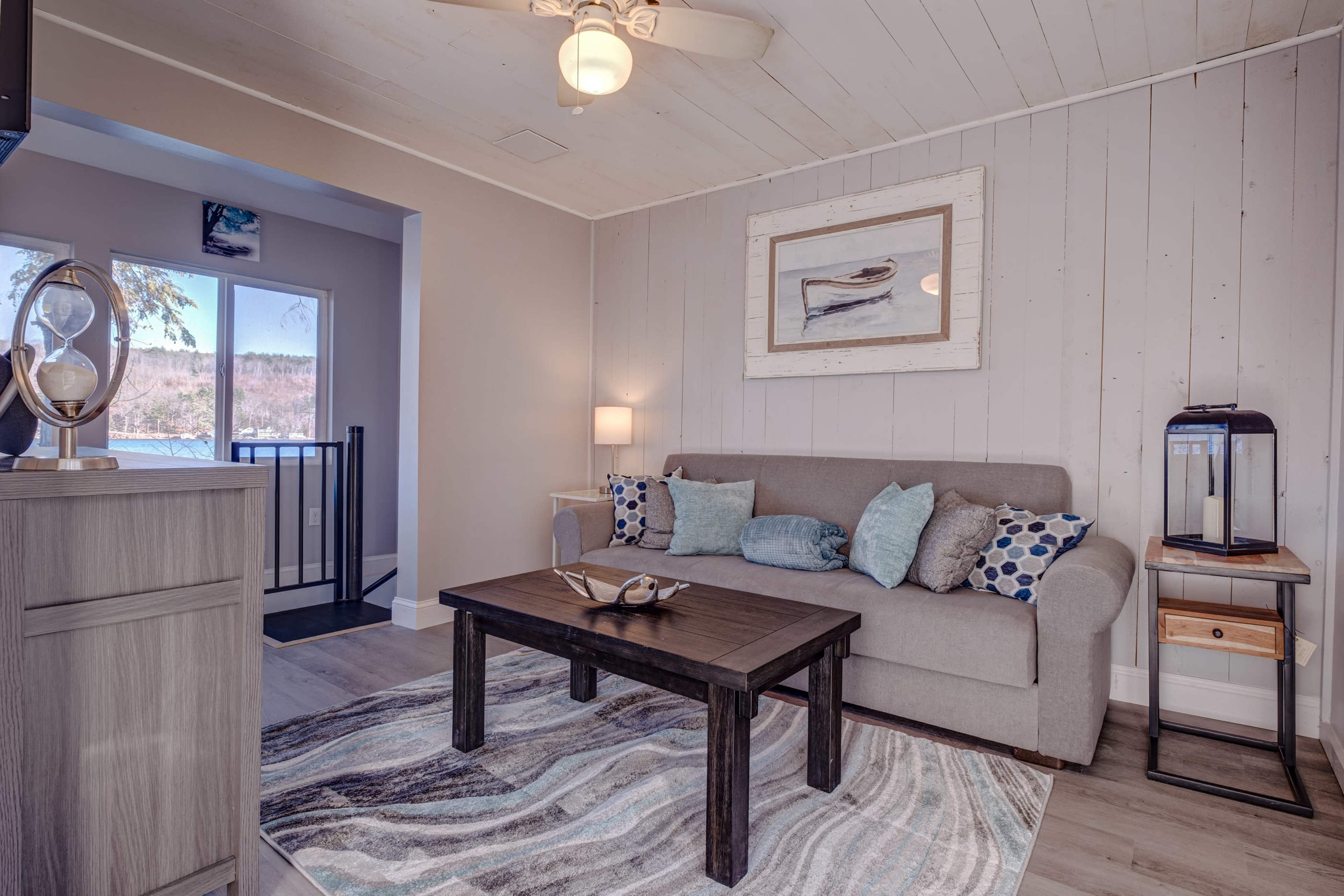 A cozy living room with a light gray sofa, a wooden coffee table, and a large window overlooking a scenic view.