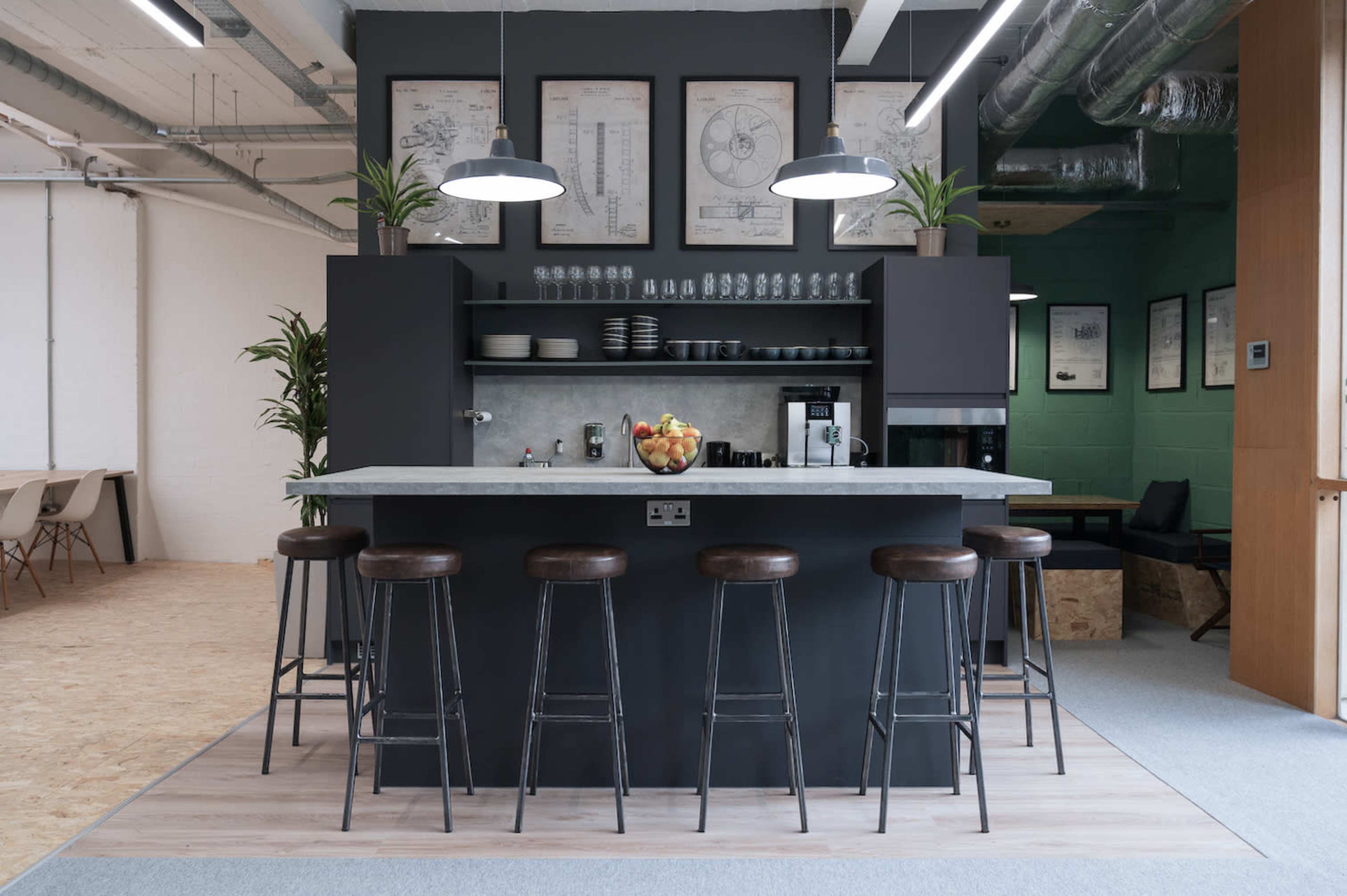 A modern kitchen area features a central island with bar stools, surrounded by shelves of dishes and plants, and framed illustrations on the walls.