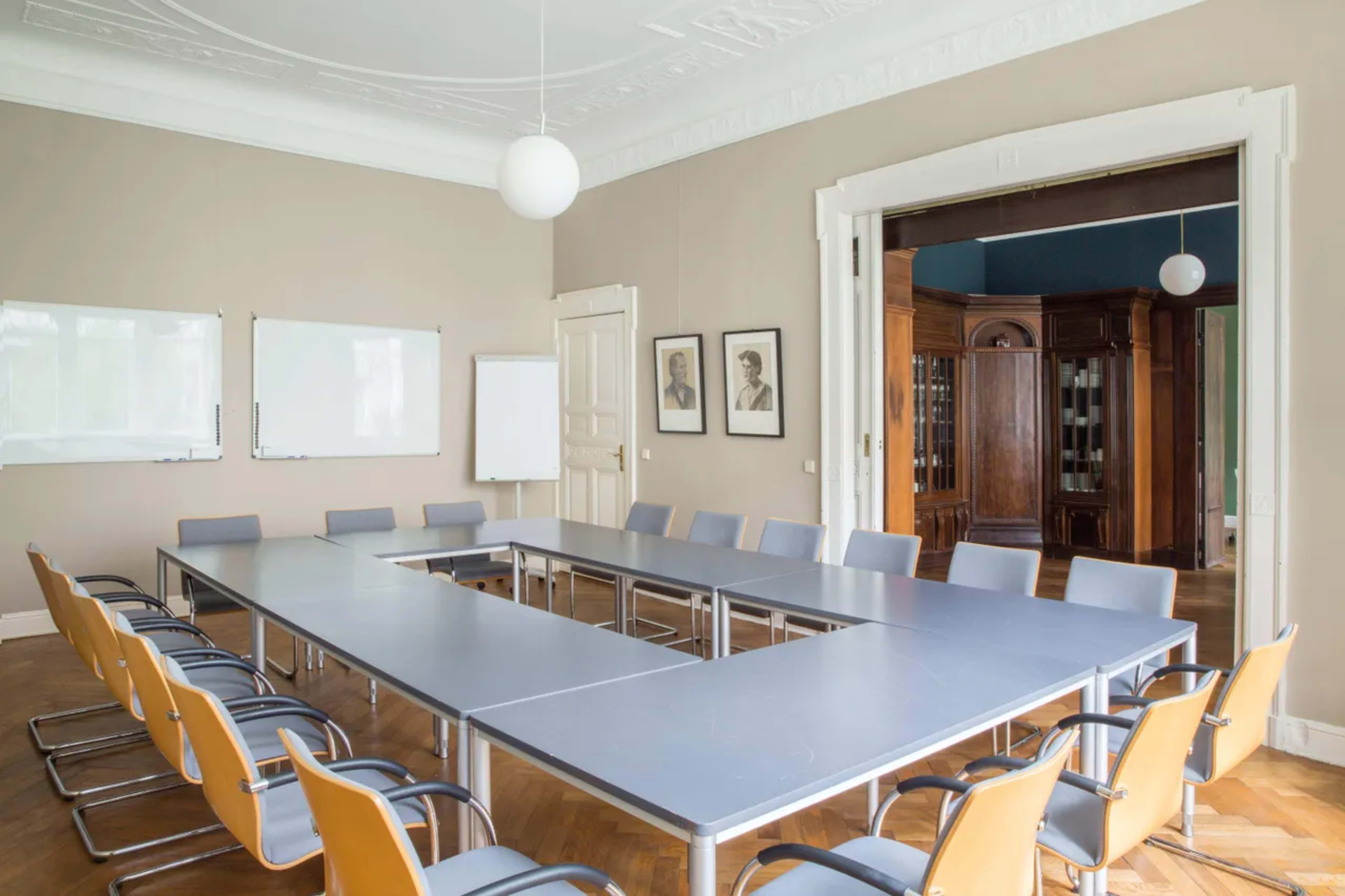 A spacious conference room with a large rectangular table surrounded by chairs and featuring whiteboards on the walls.