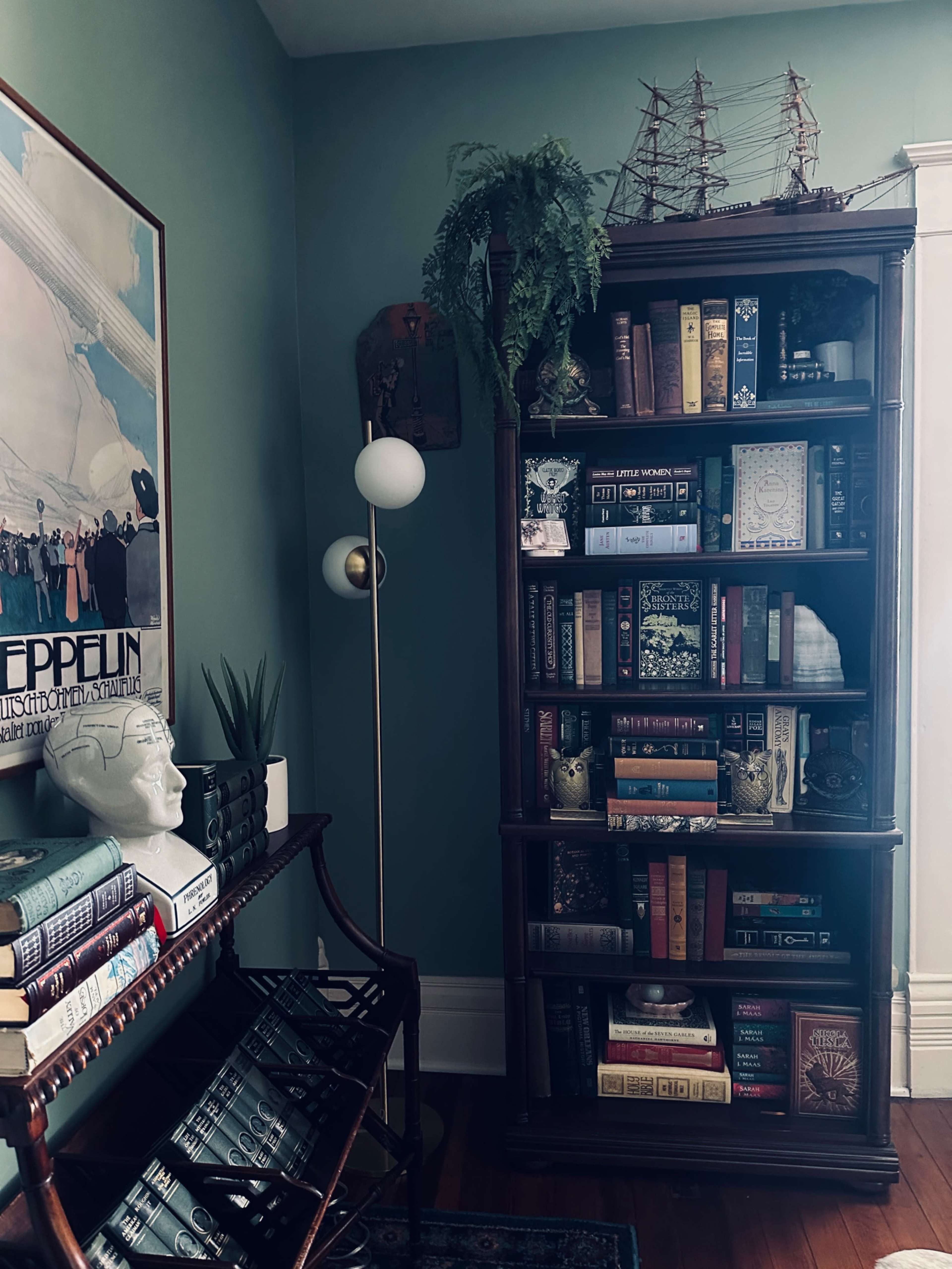 A wooden bookshelf filled with books and decorative items stands in a corner of a room, alongside a floor lamp and a small table.