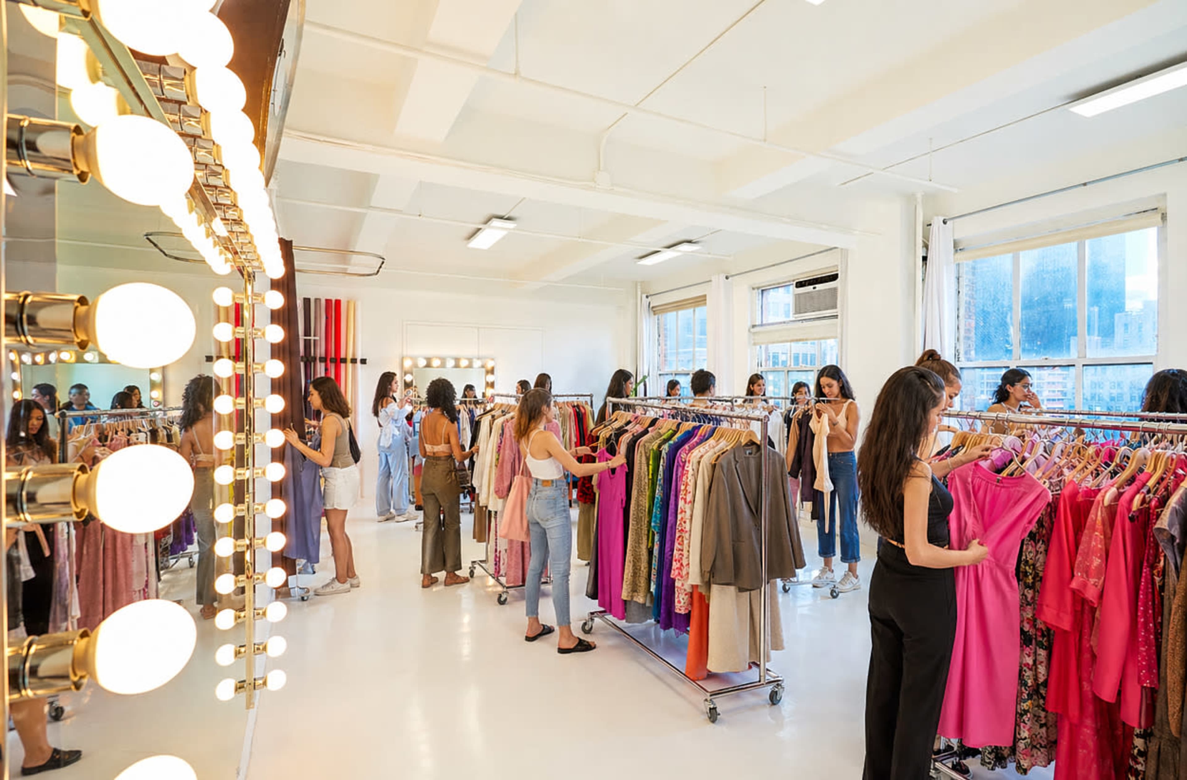 A group of people browse through clothing racks in a brightly lit fashion studio.