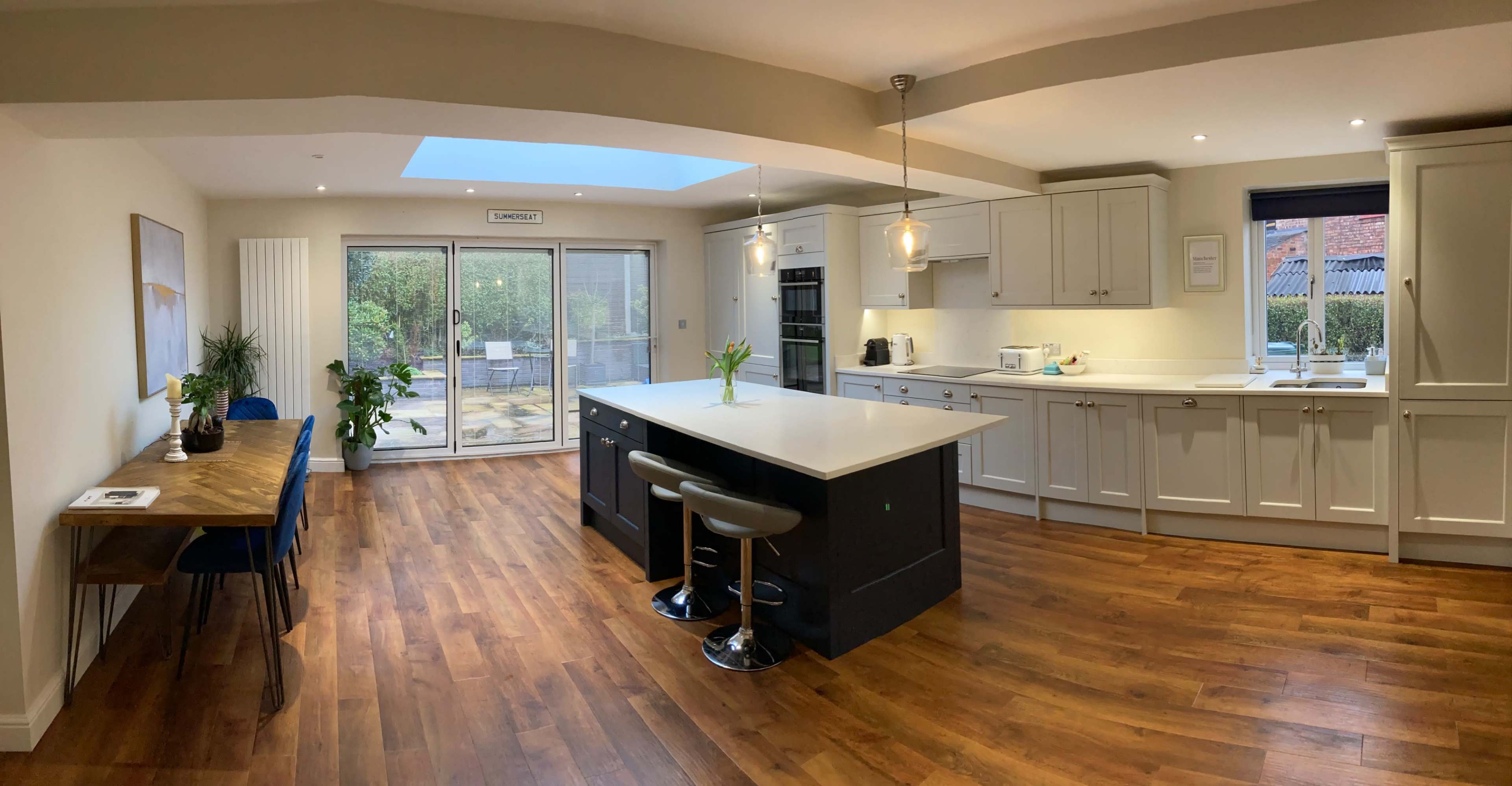 A modern kitchen features an island with seating, wooden flooring, and large sliding doors leading to an outdoor patio.