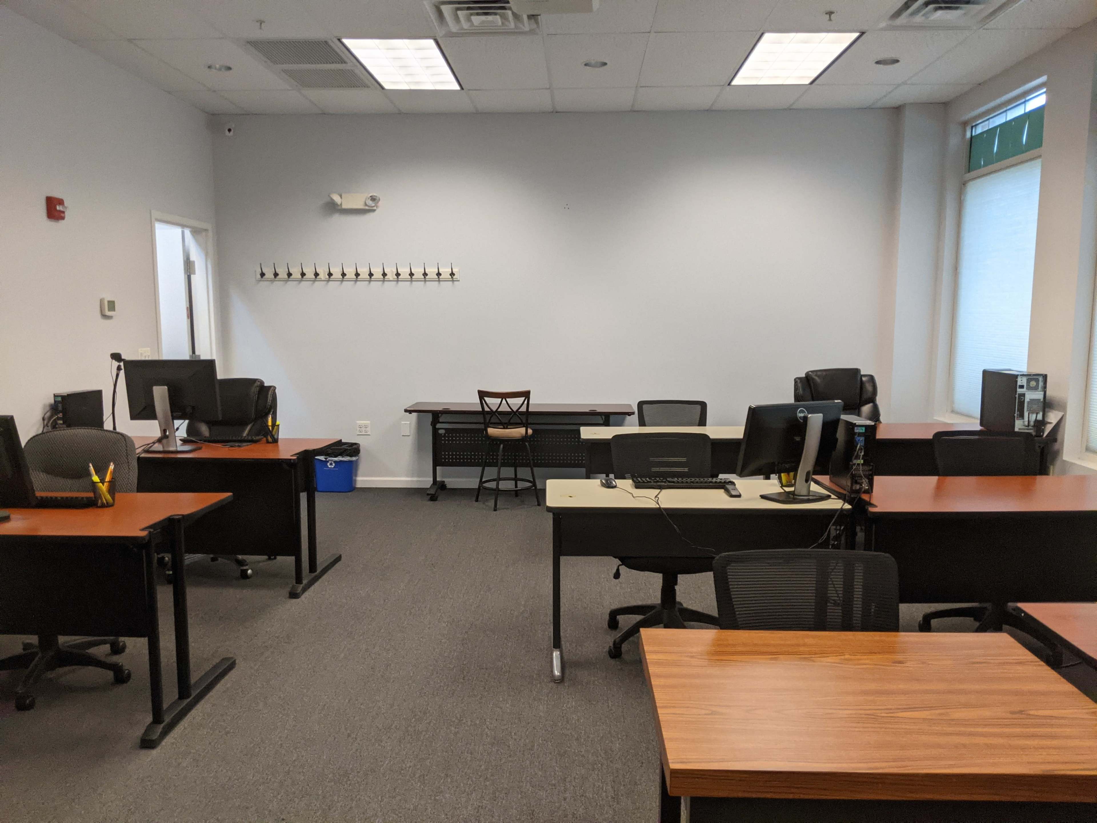 A sparsely furnished office space with several desks, chairs, and two computer stations.