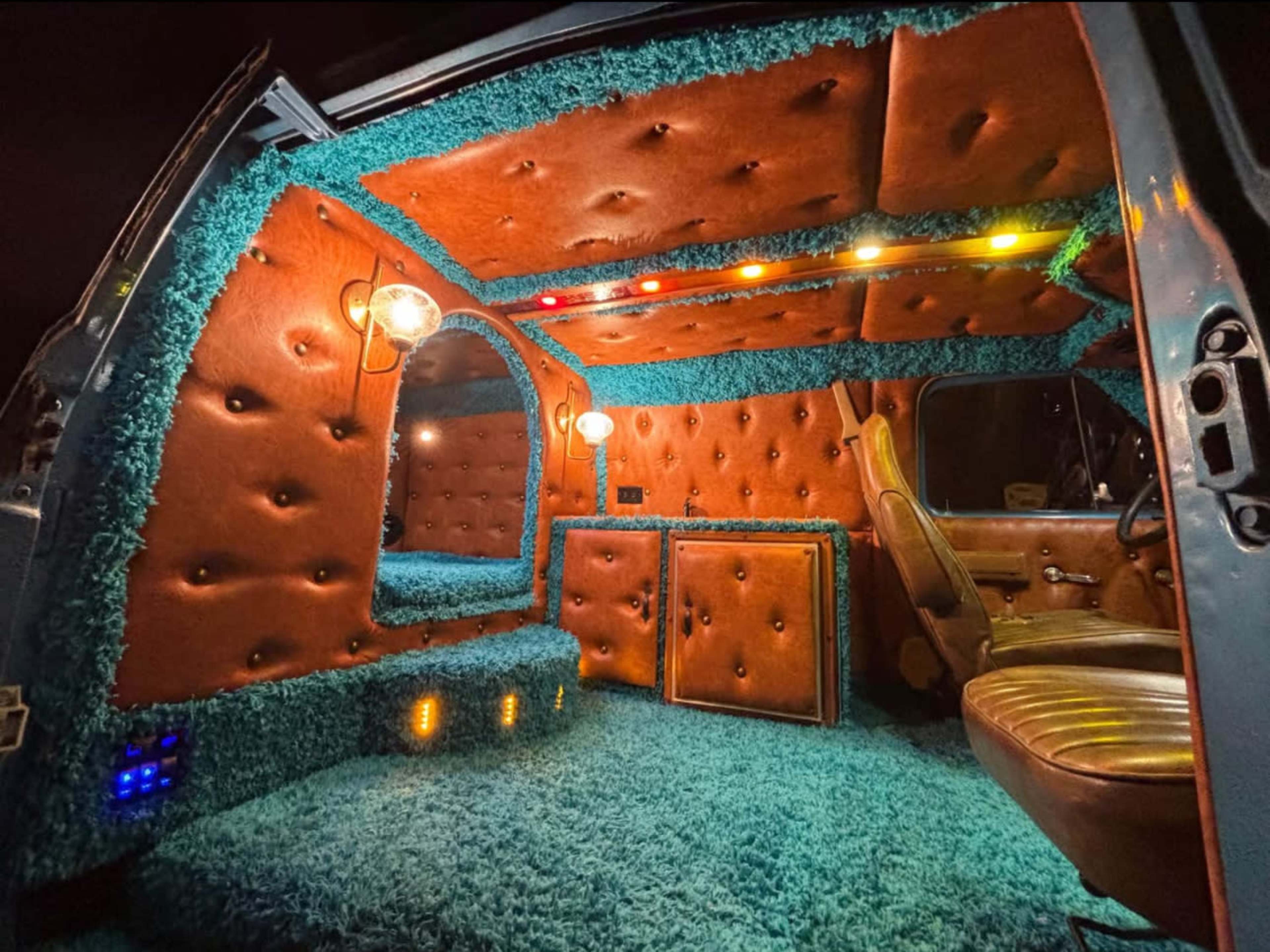 The interior of a van is lined with plush brown panels and vibrant turquoise carpeting, featuring unique lighting elements.