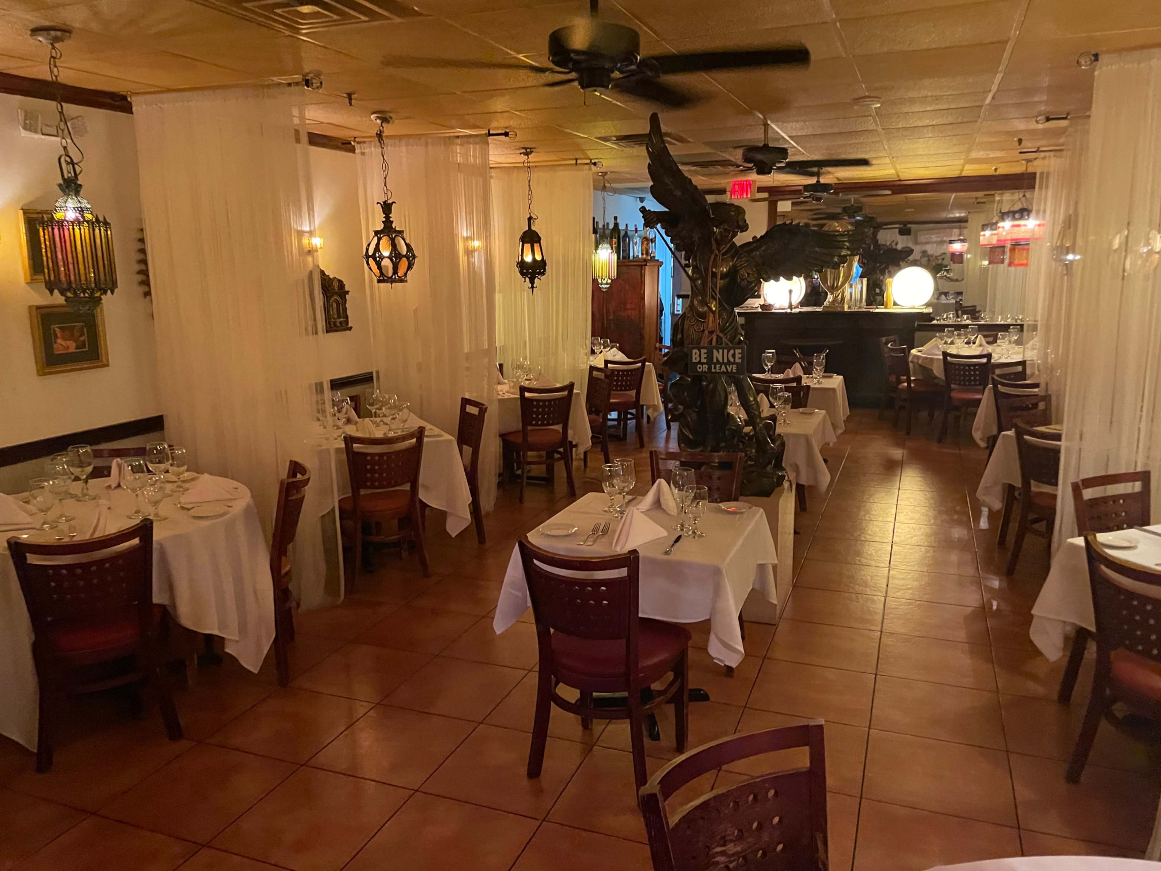 A dining area of a restaurant featuring white tablecloths, wooden chairs, and decorative lighting.