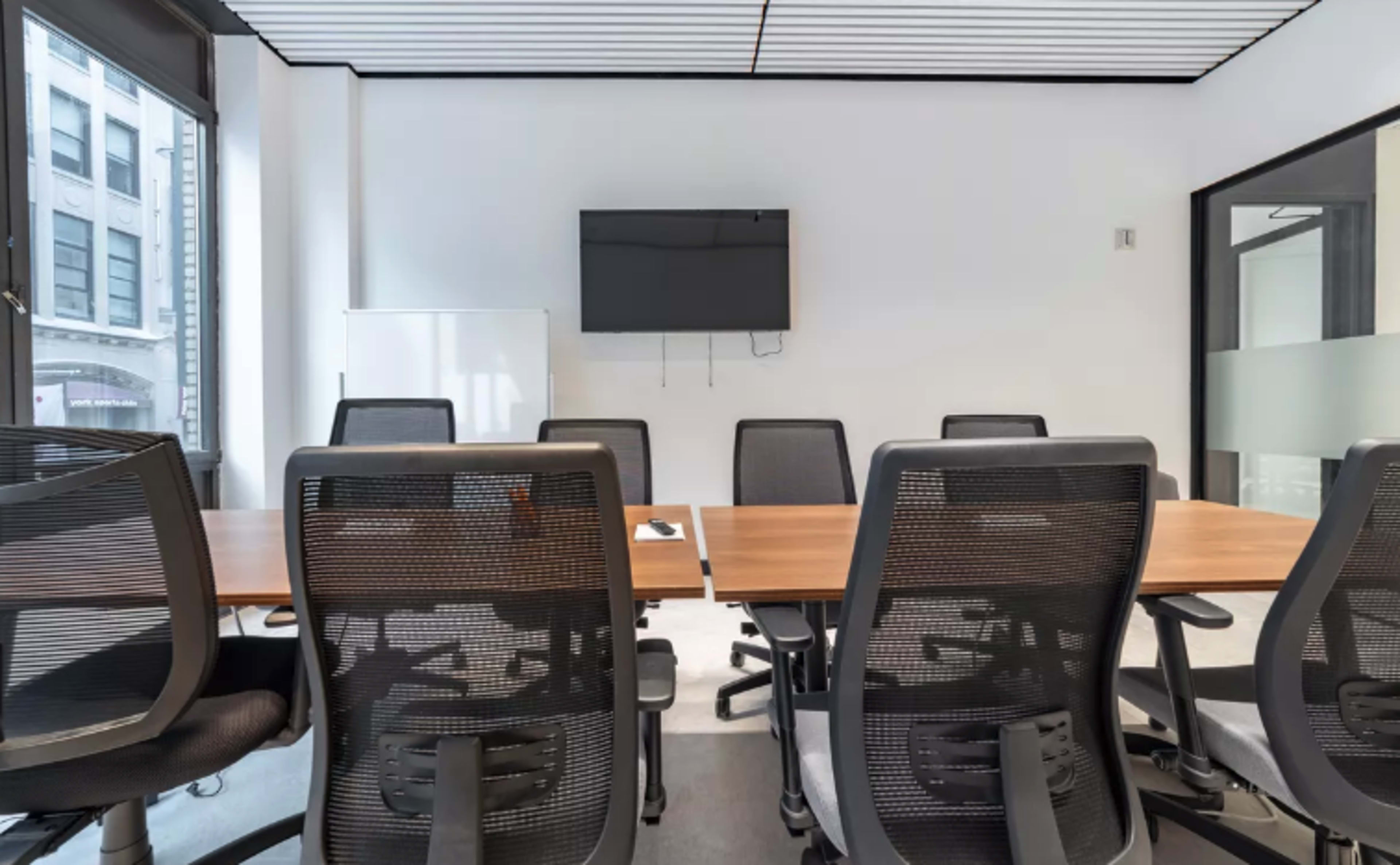 A modern conference room with a long table, several ergonomic chairs, and a wall-mounted television.