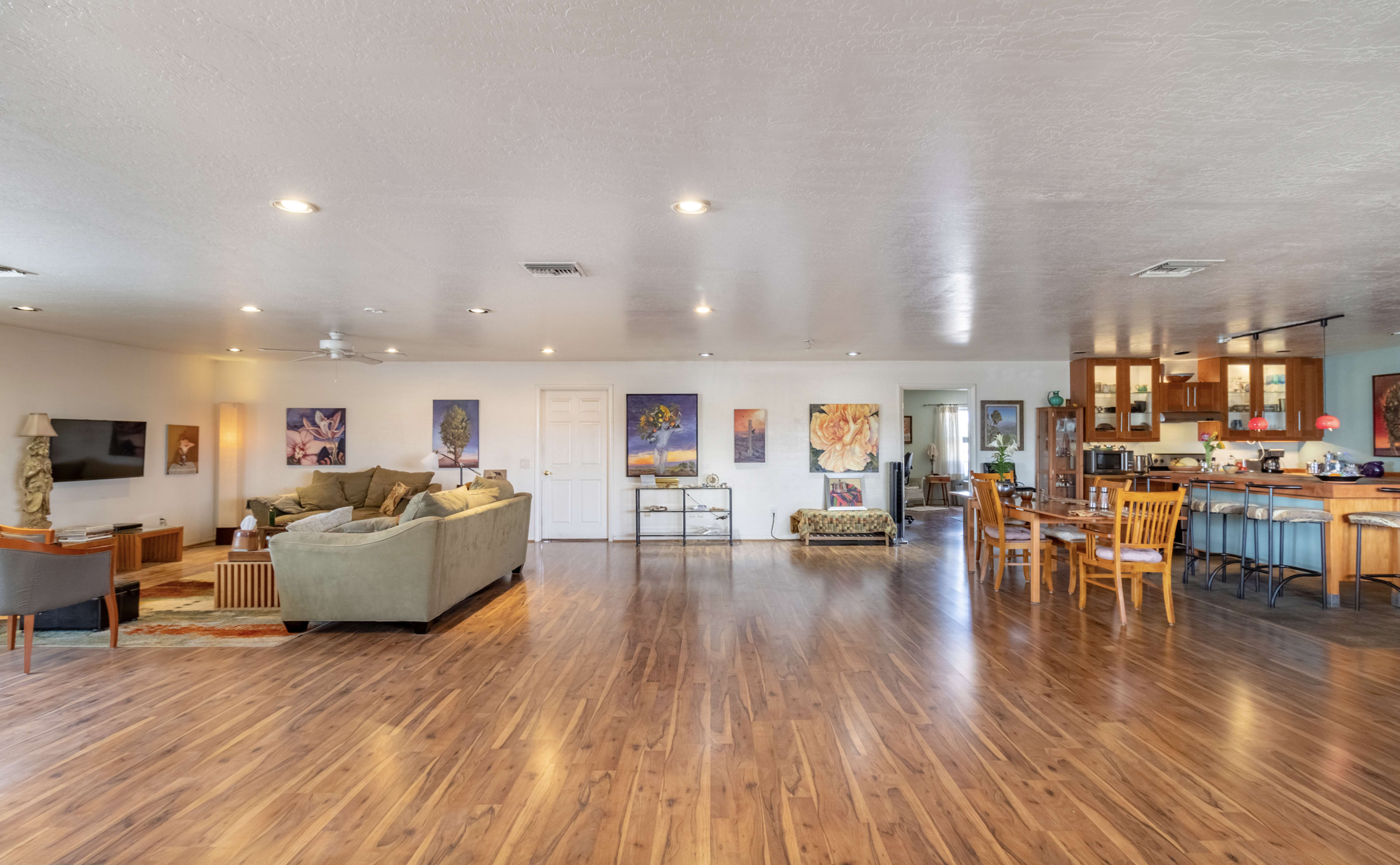A spacious living area features a green sofa, wooden dining set, and a kitchen with wooden cabinets, all illuminated by overhead lights.