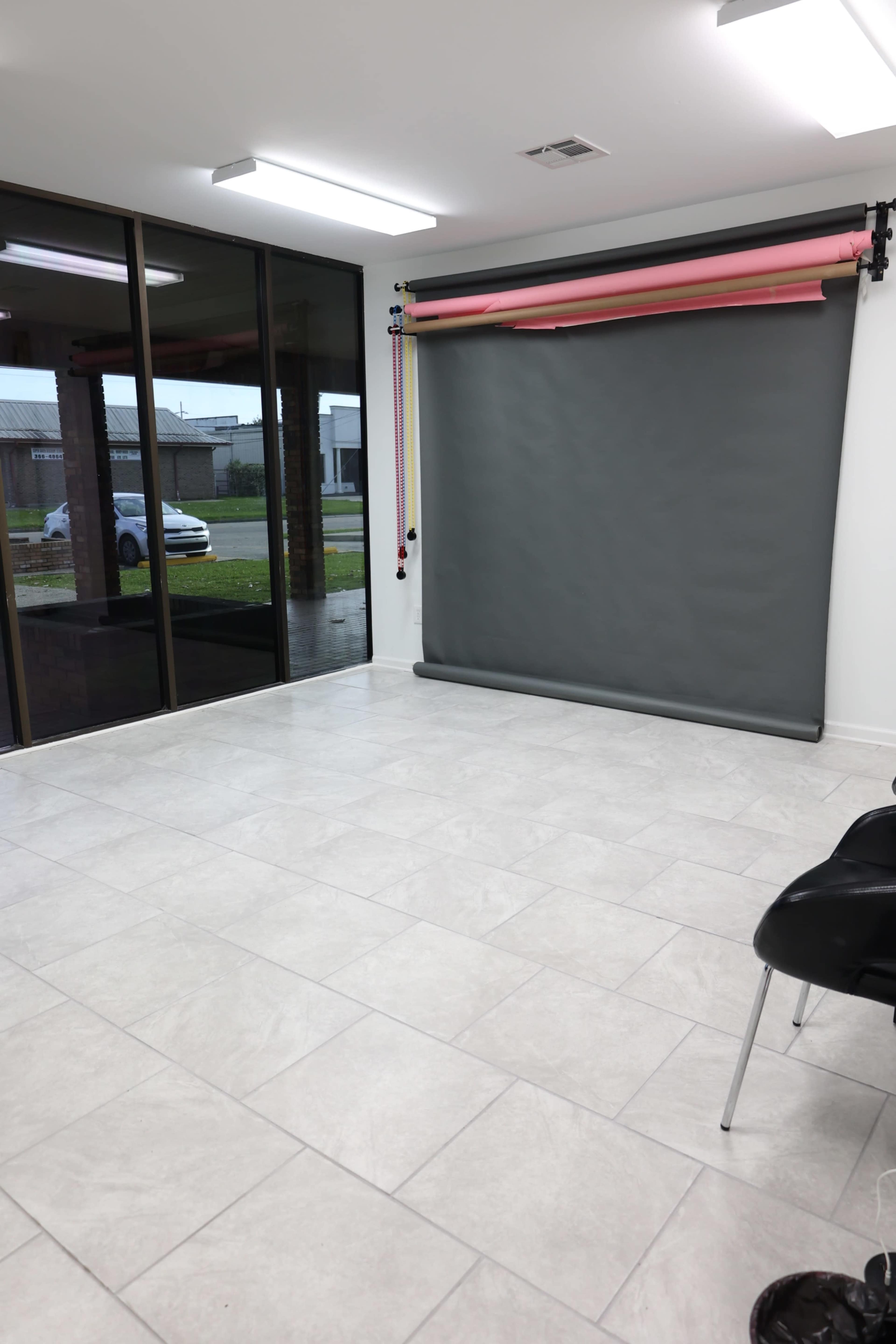 The image shows a spacious room with tiled flooring, a gray backdrop on a roll-up stand, and a large glass door that opens to an outdoor view.