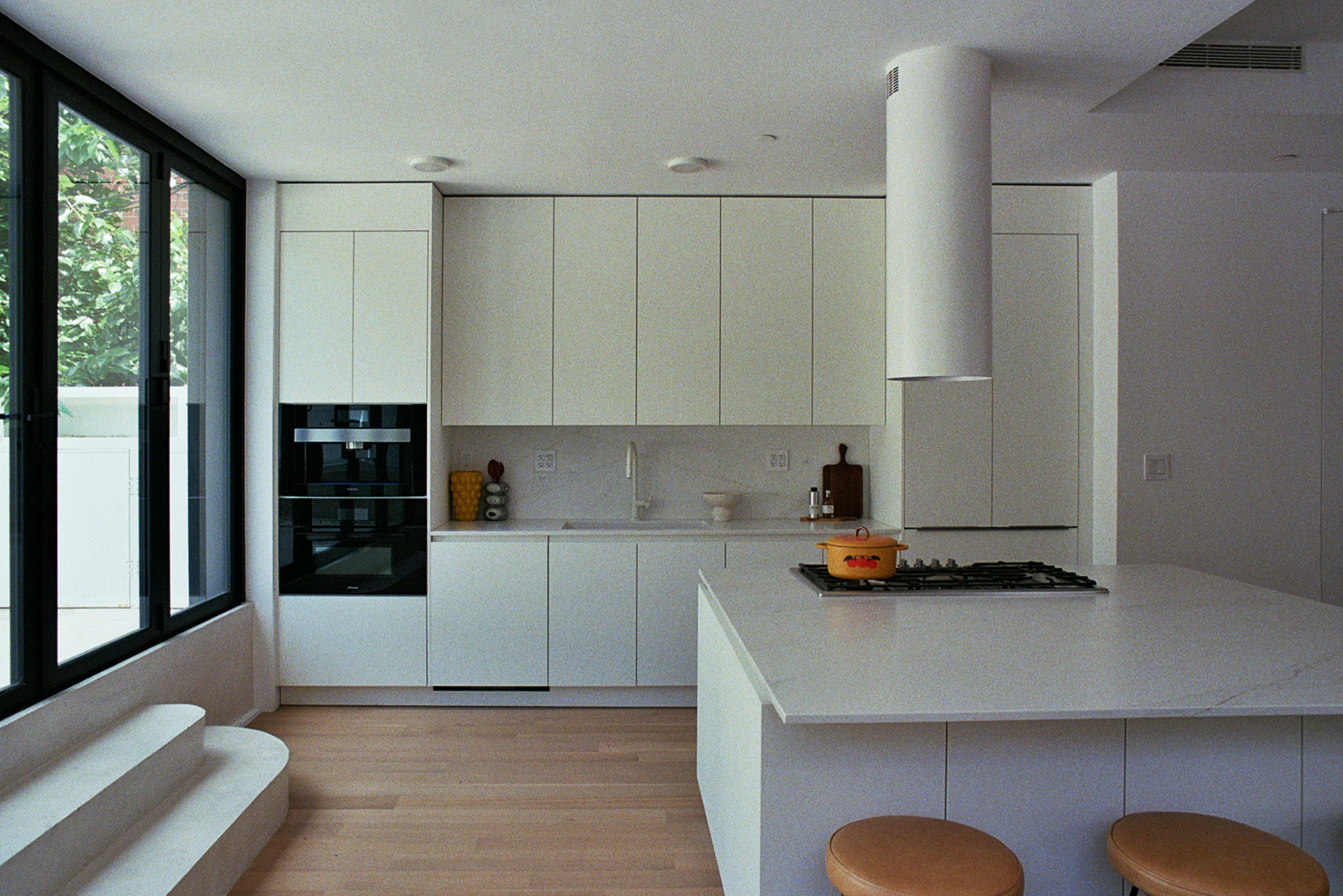A modern kitchen features white cabinetry, a central island, a gas stove, and large windows allowing natural light to enter.