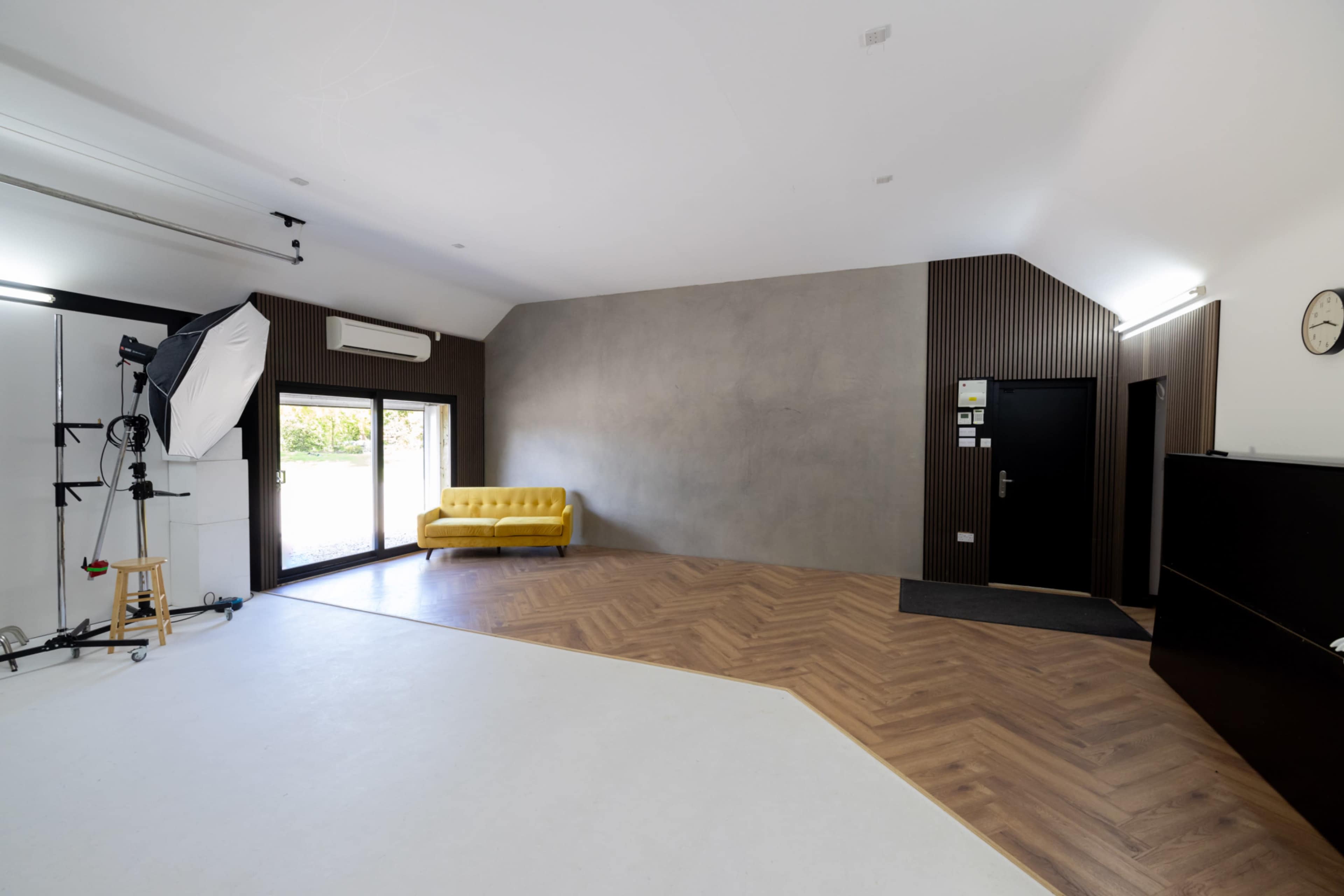 A minimalist interior room featuring a yellow sofa, large windows, and a wooden floor with an area of white flooring.