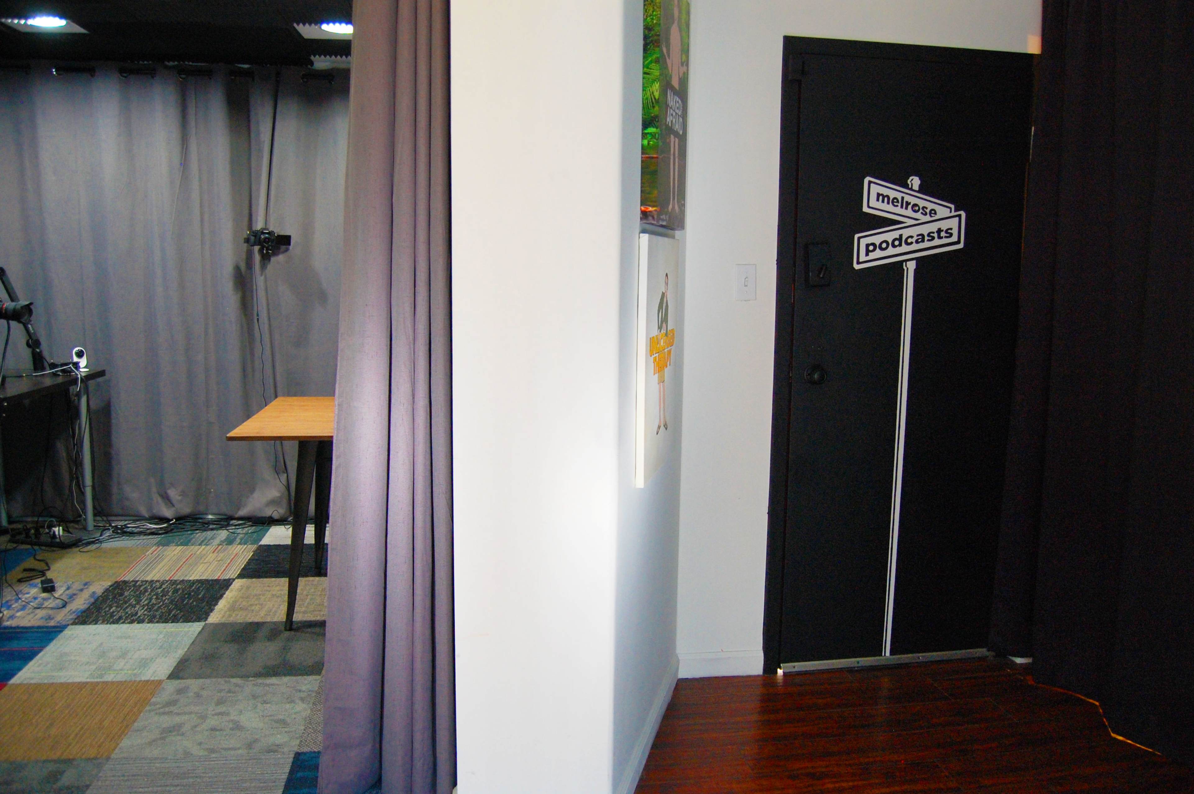A corridor leading to a door marked "podcasts," with a tabletop visible in the adjacent room behind a curtain.