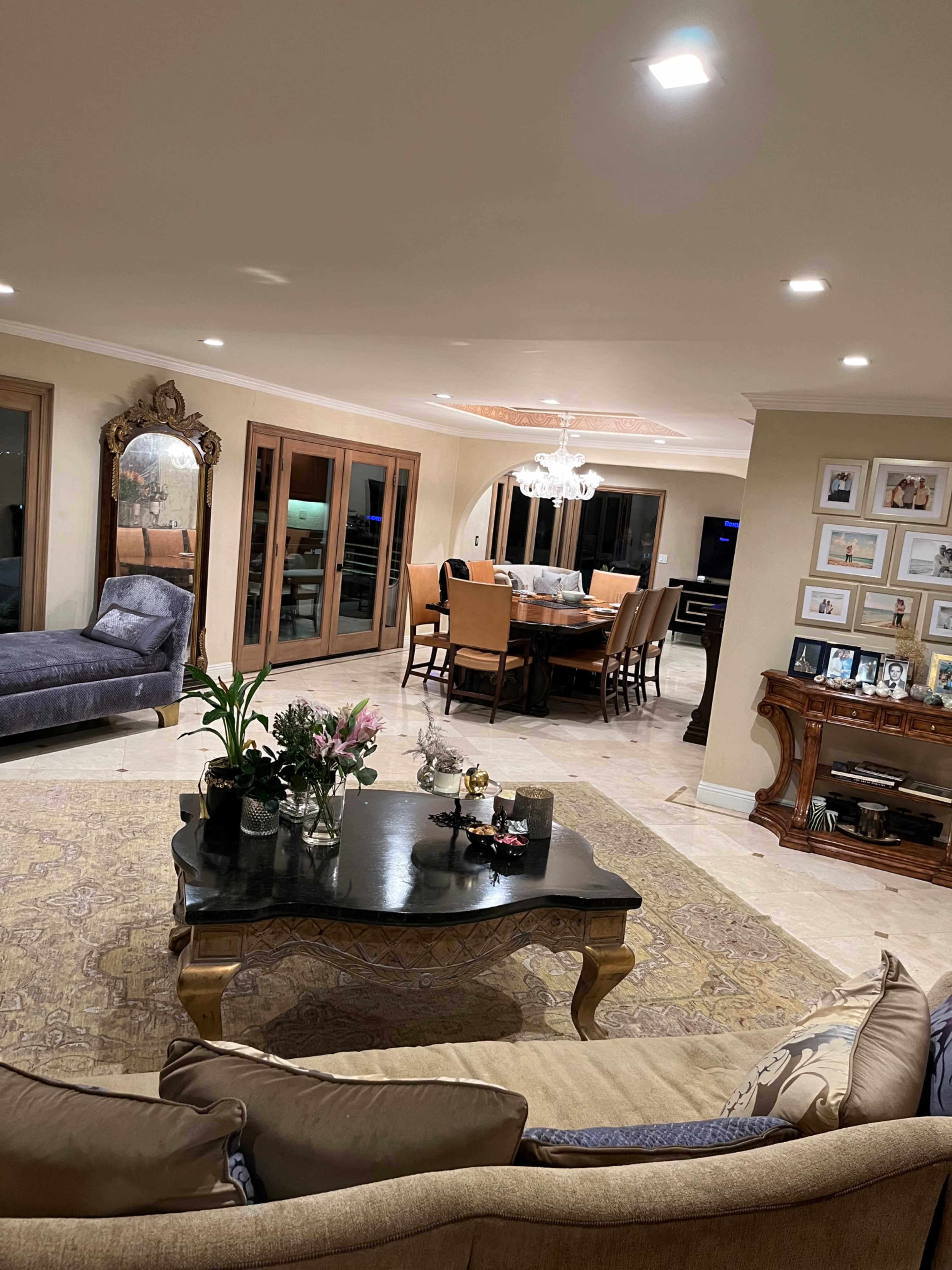 A spacious living room features a dining area with a large table, elegant lighting, and a mix of comfortable seating arrangements.