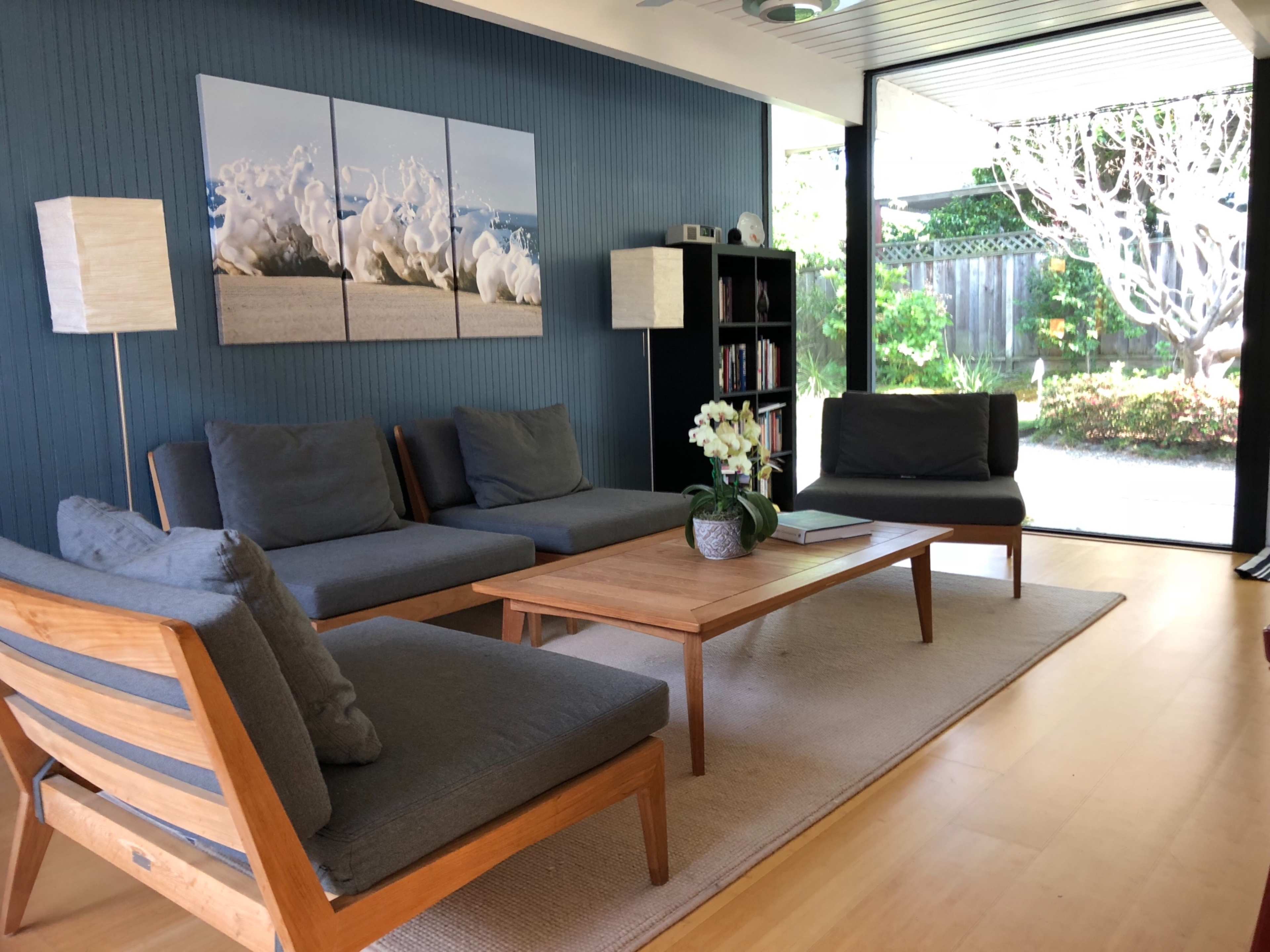 A modern living room features gray sofas, a wooden coffee table, and large windows overlooking a garden.