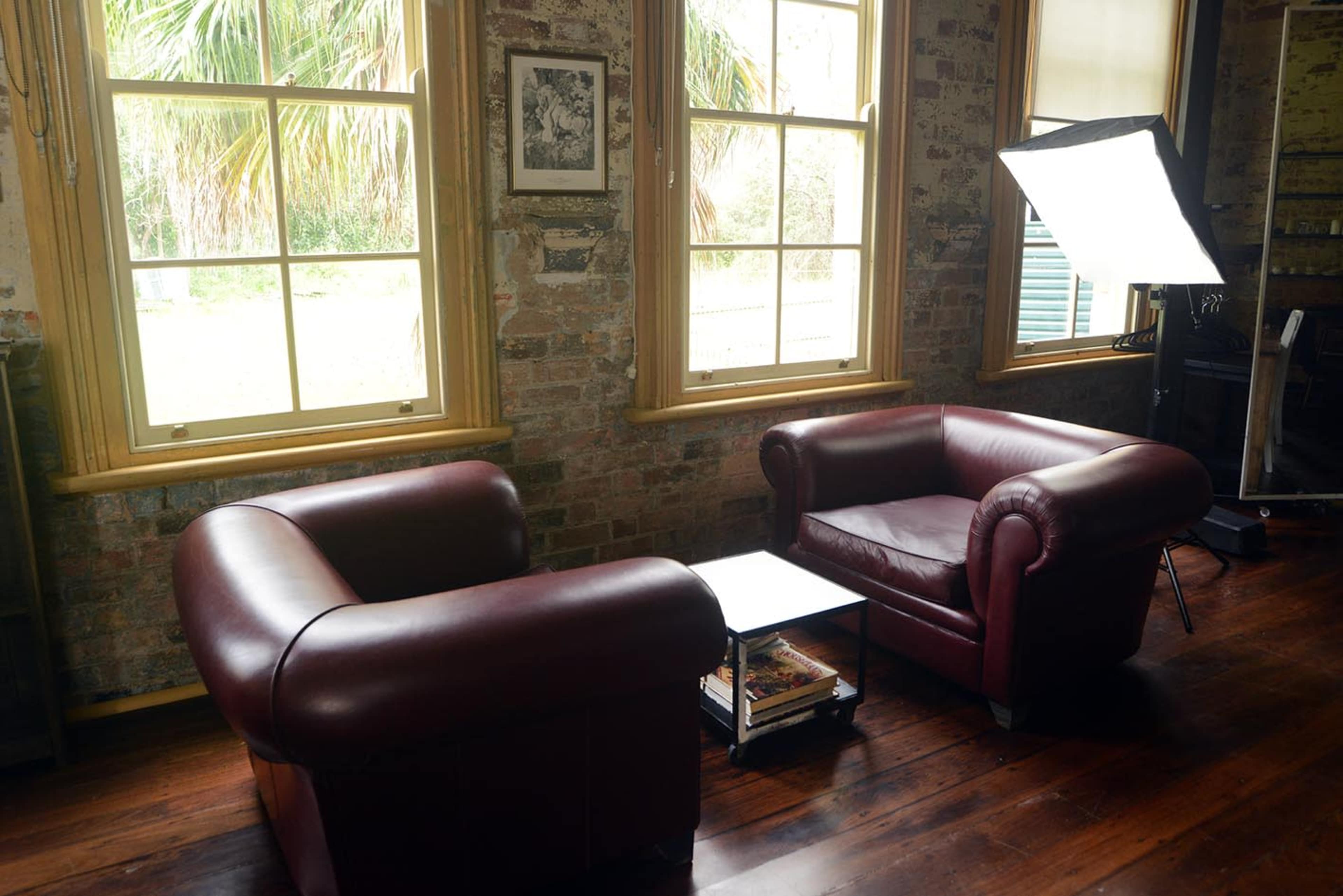 Two burgundy leather armchairs facing each other in a room with large windows and exposed brick walls.