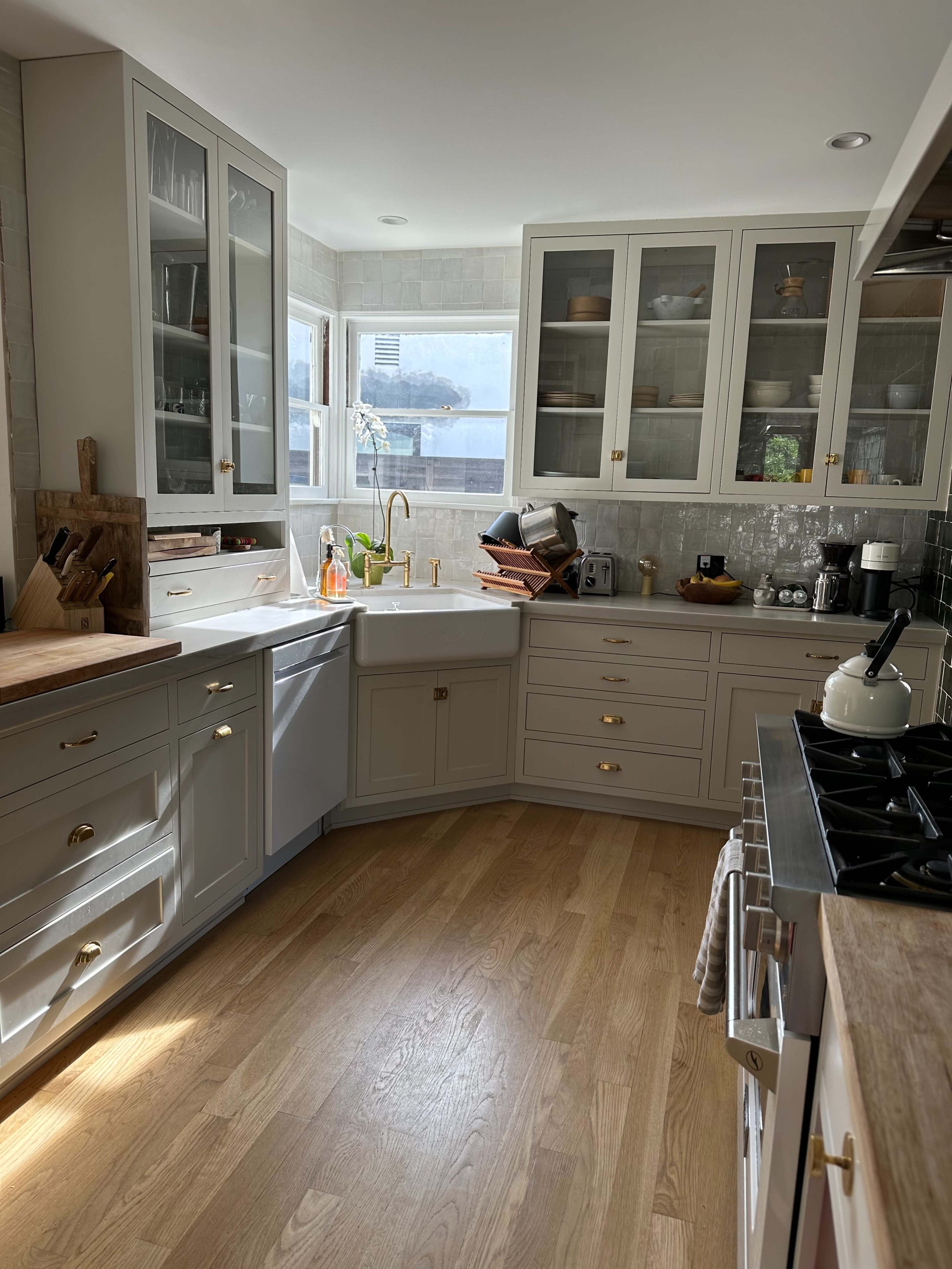 A modern kitchen with gray cabinetry, a double bowl sink, and a window allowing natural light to illuminate the wooden floor.