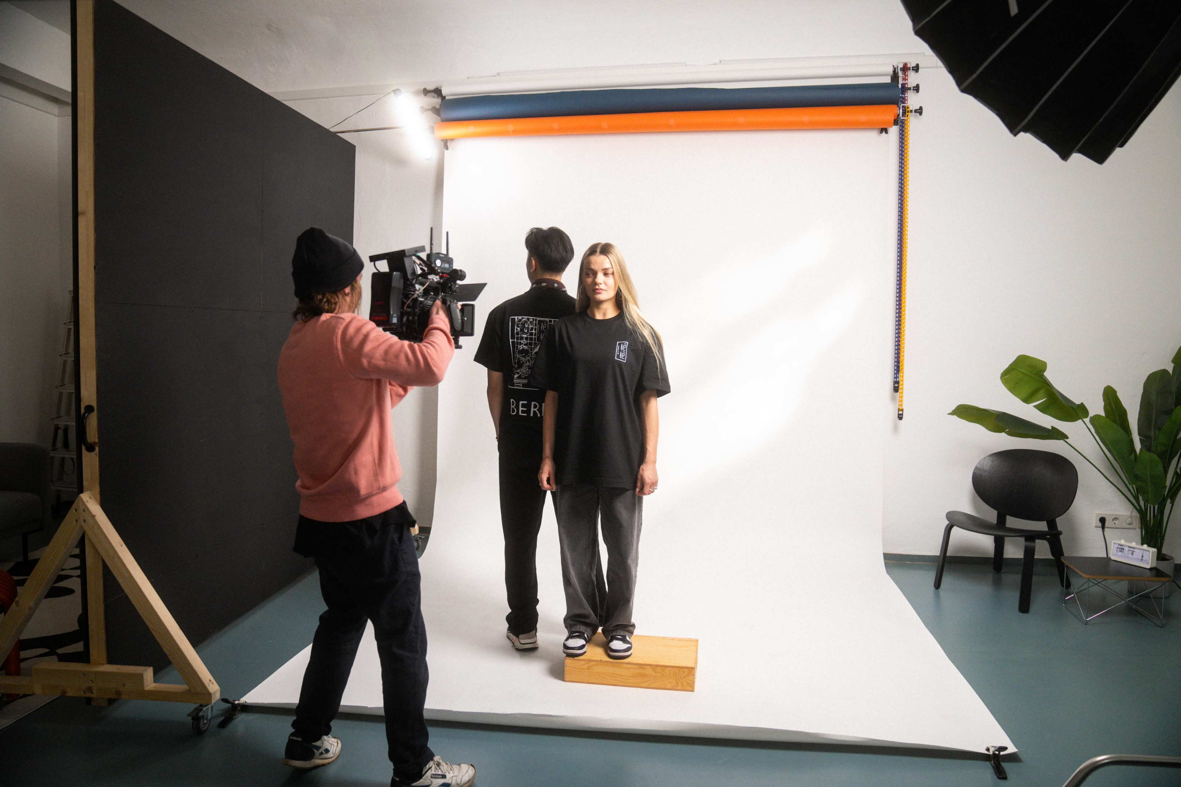 A photographer captures a model standing on a platform in a studio with a plain white backdrop.