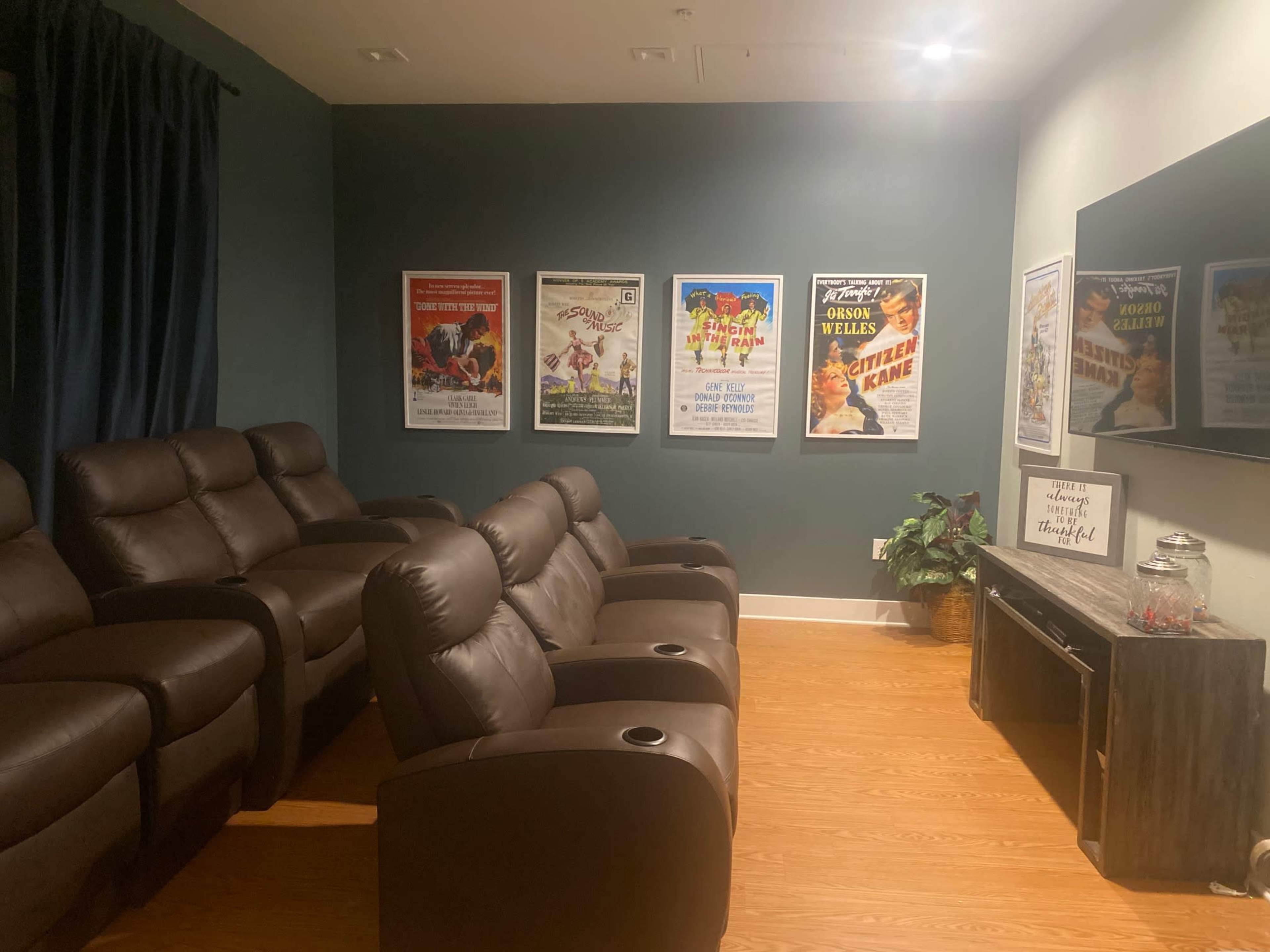 A home theater features leather recliners arranged in front of a television and walls adorned with retro movie posters.