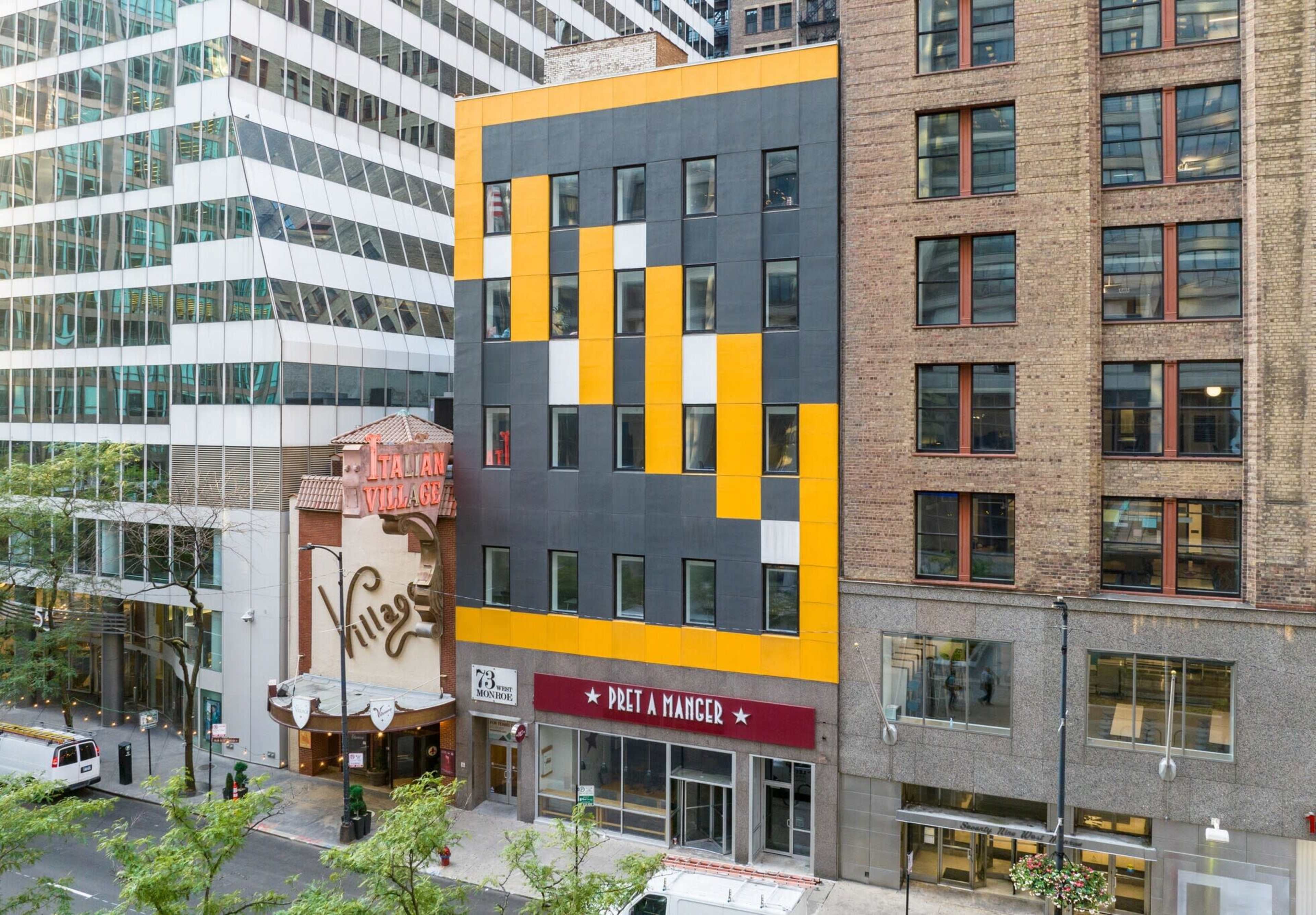 The image shows a modern building with a black and yellow façade, located next to a theater with a marquee sign in a city setting.