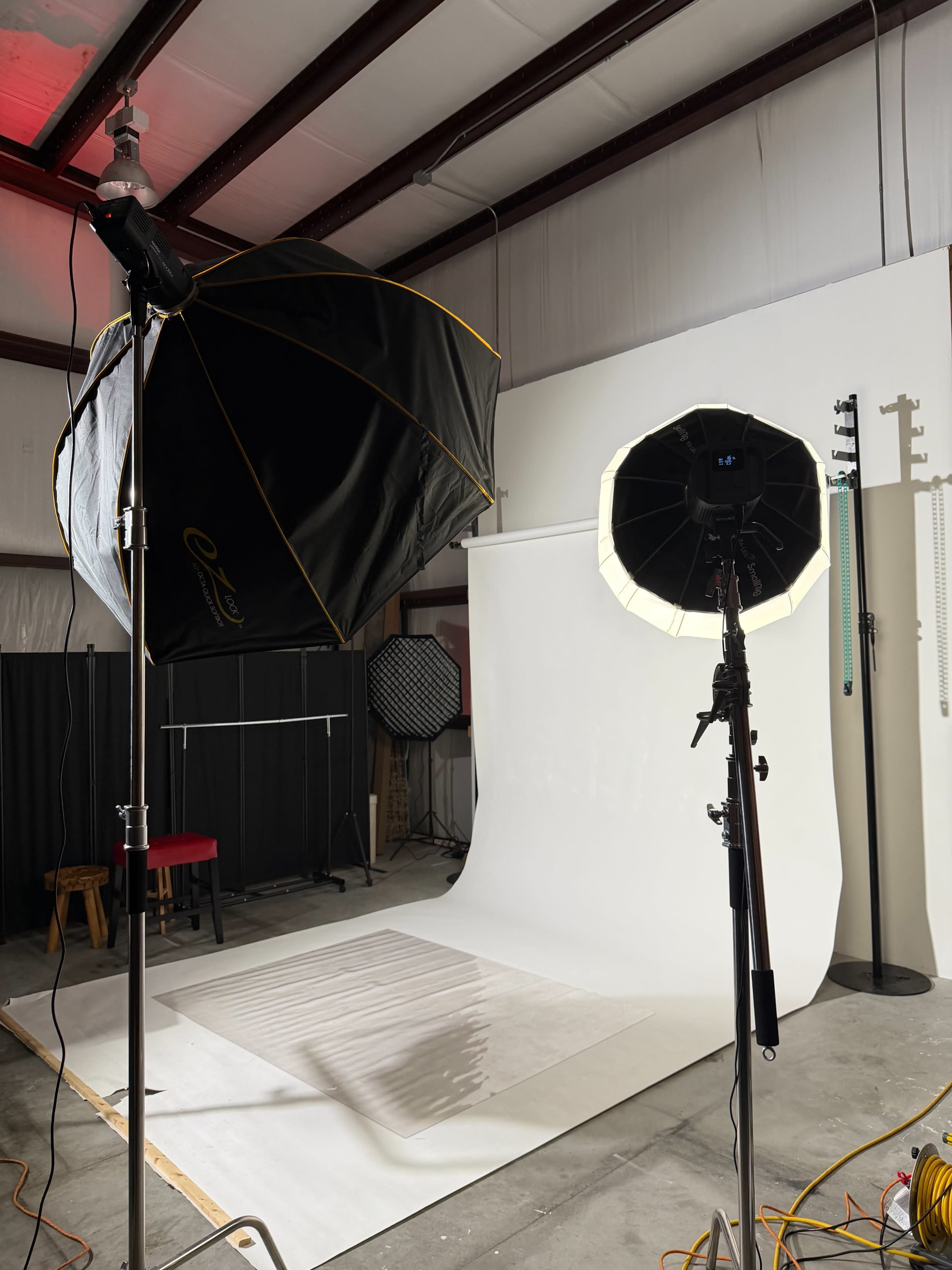 A photography studio is set up with softbox and ring lights illuminating a backdrop area with a white seamless background.