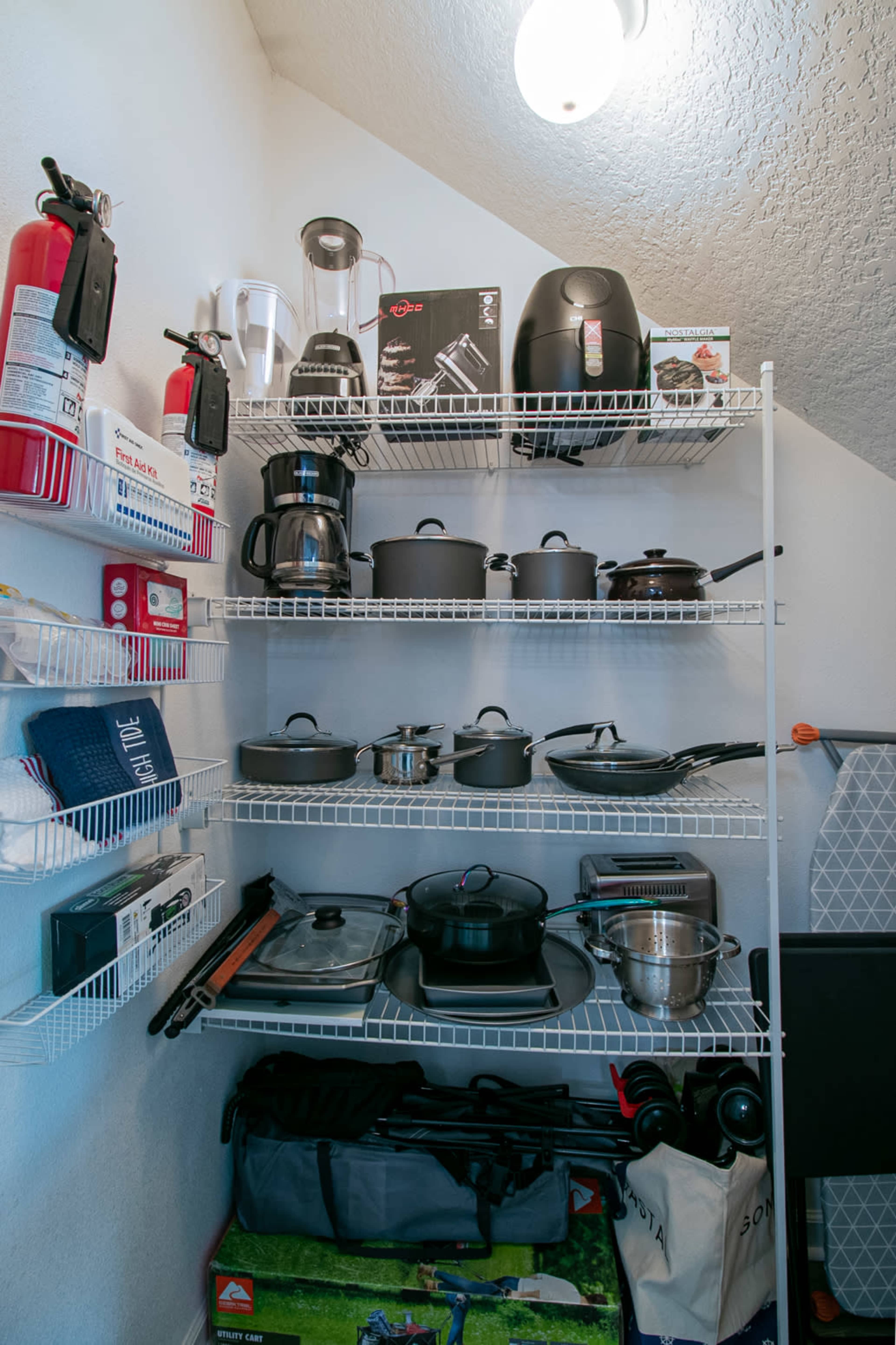 A neatly organized shelving unit displays various kitchen appliances, cookware, and utensils, alongside fire extinguishers and additional storage items.