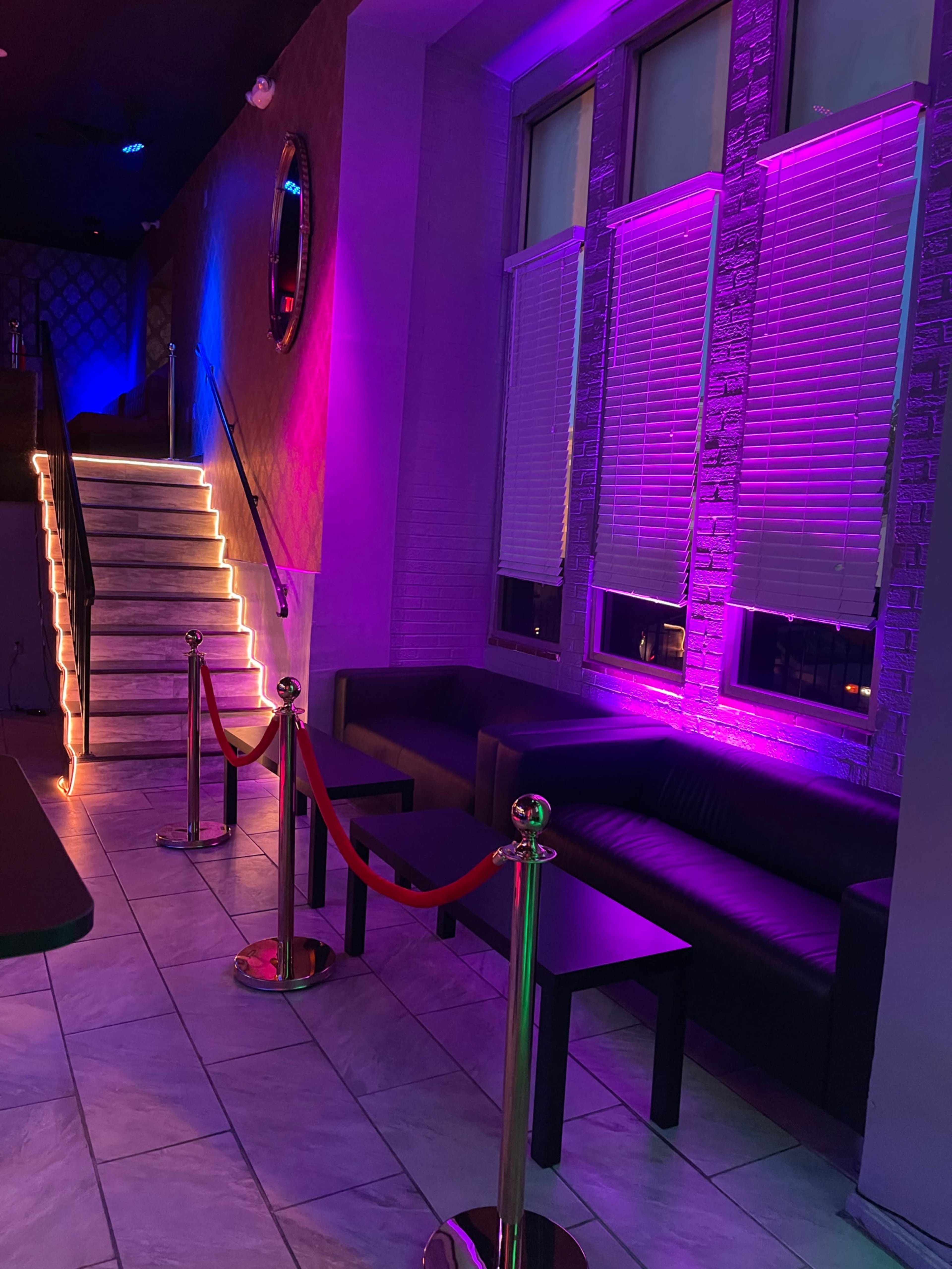 The interior features a staircase illuminated with LED lights, flanked by sectional couches and velvet rope barriers.