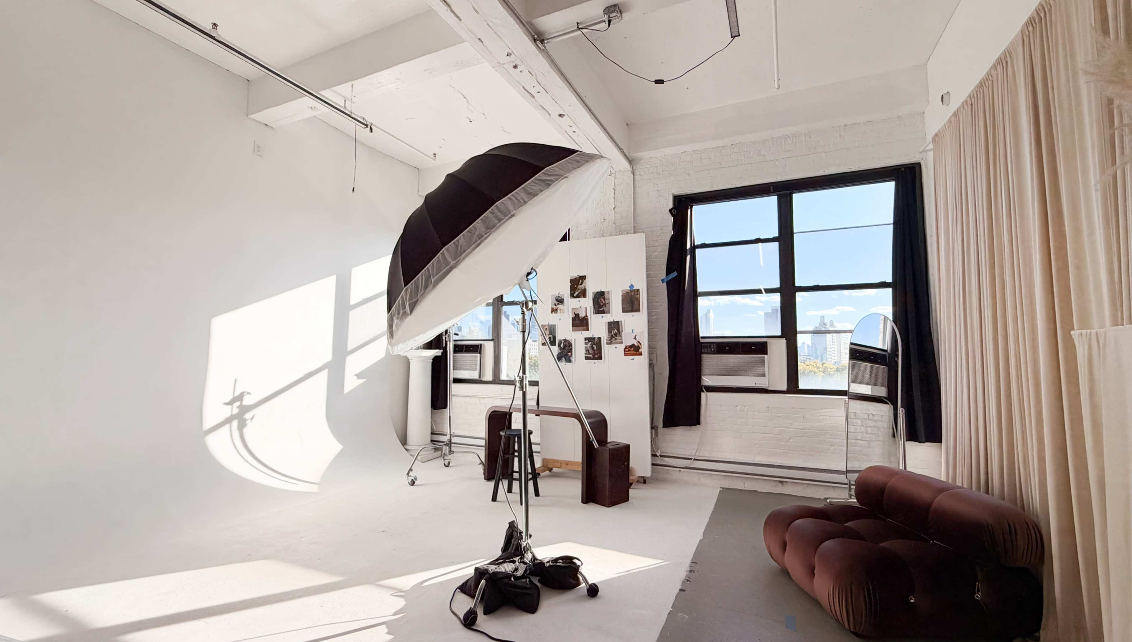 The image shows a well-lit photography studio featuring a large softbox light, a brown sofa, and a wall with photographs.