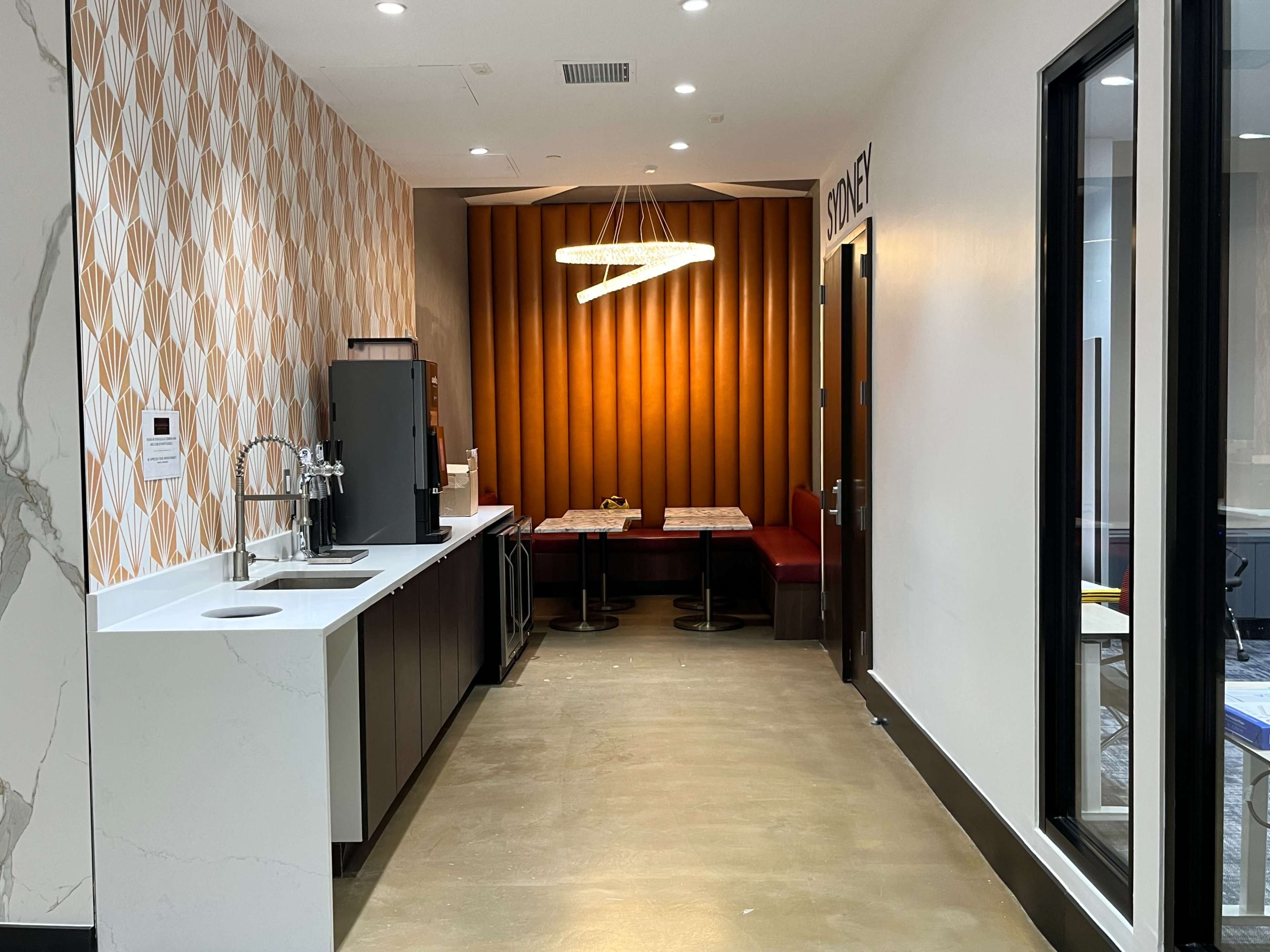 A modern break room with a kitchen area on the left and a cozy seating nook with a table on the right, accented by a decorative wall and pendant lighting.