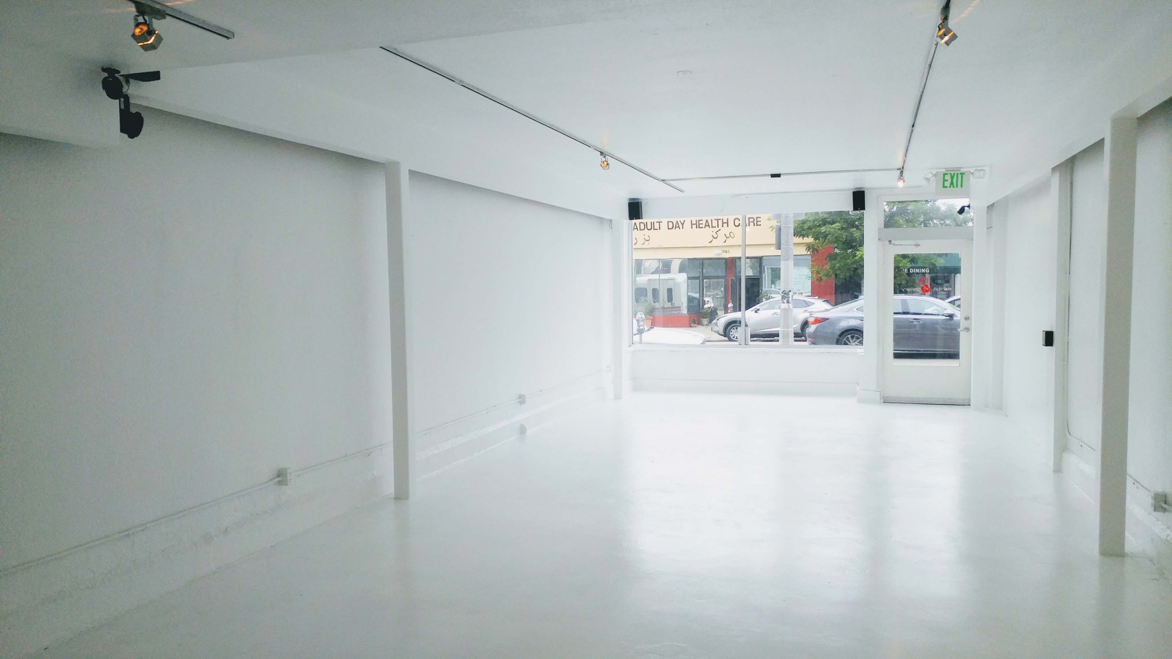 The image shows a spacious, empty room with white walls, a polished floor, and a large window facing a street.
