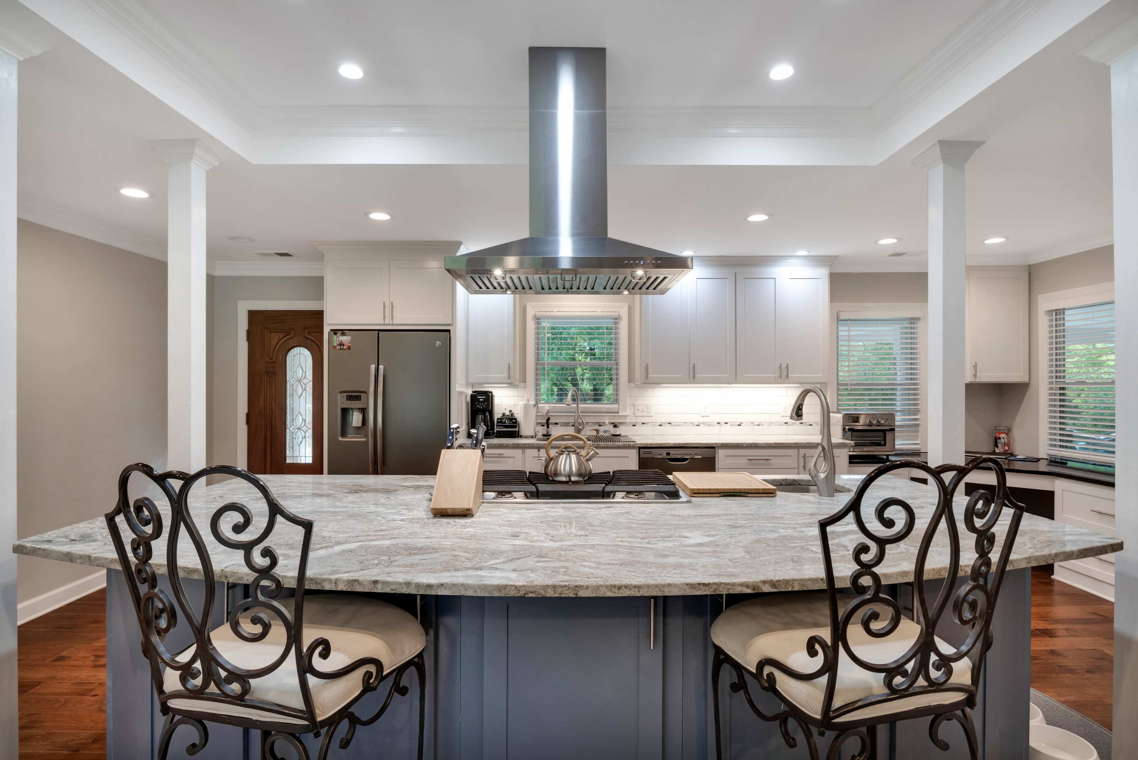 A modern kitchen features a central island with bar seating, stainless steel appliances, and a range hood above the cooktop.