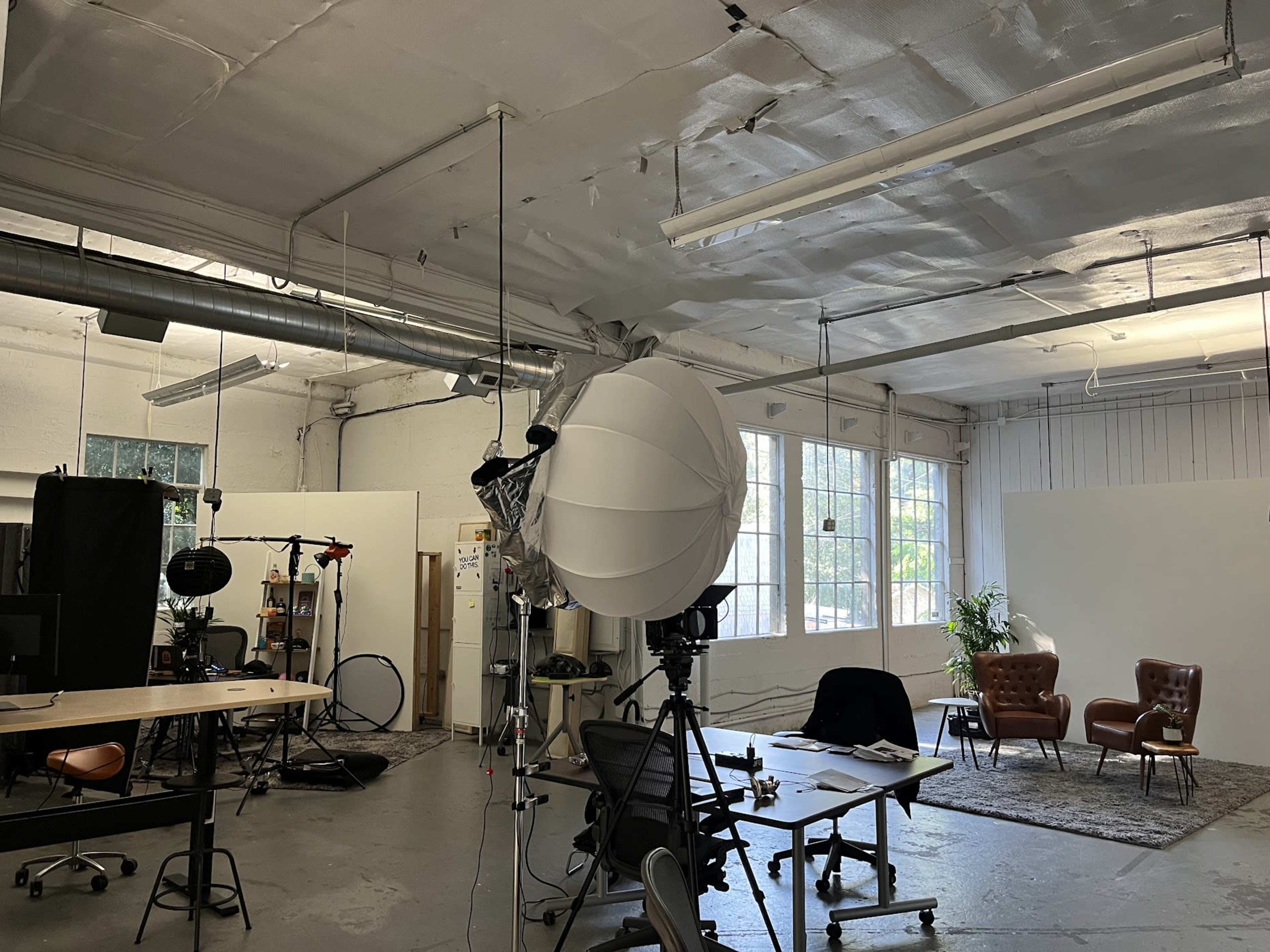 A spacious studio with a large softbox light, a desk, chairs, and a backdrop setup for photography or video production.