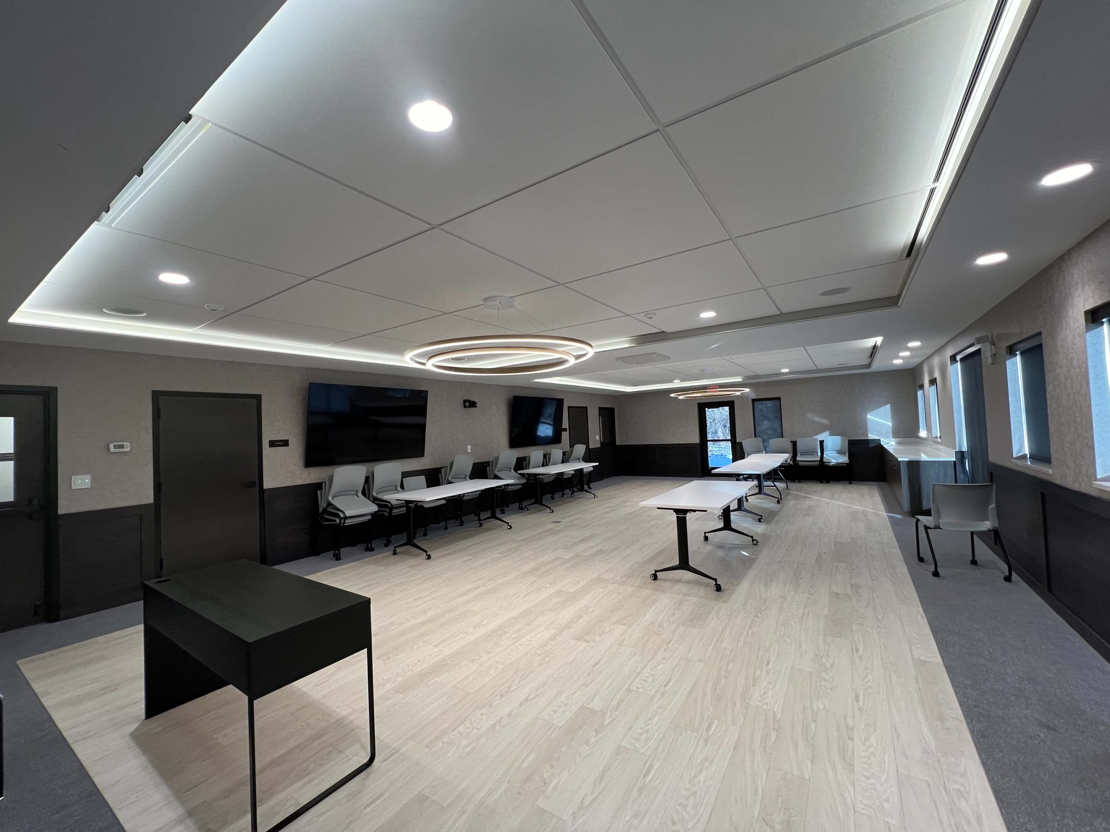 A modern conference room featuring a large oval light fixture, multiple tables, and chairs arranged for meetings.