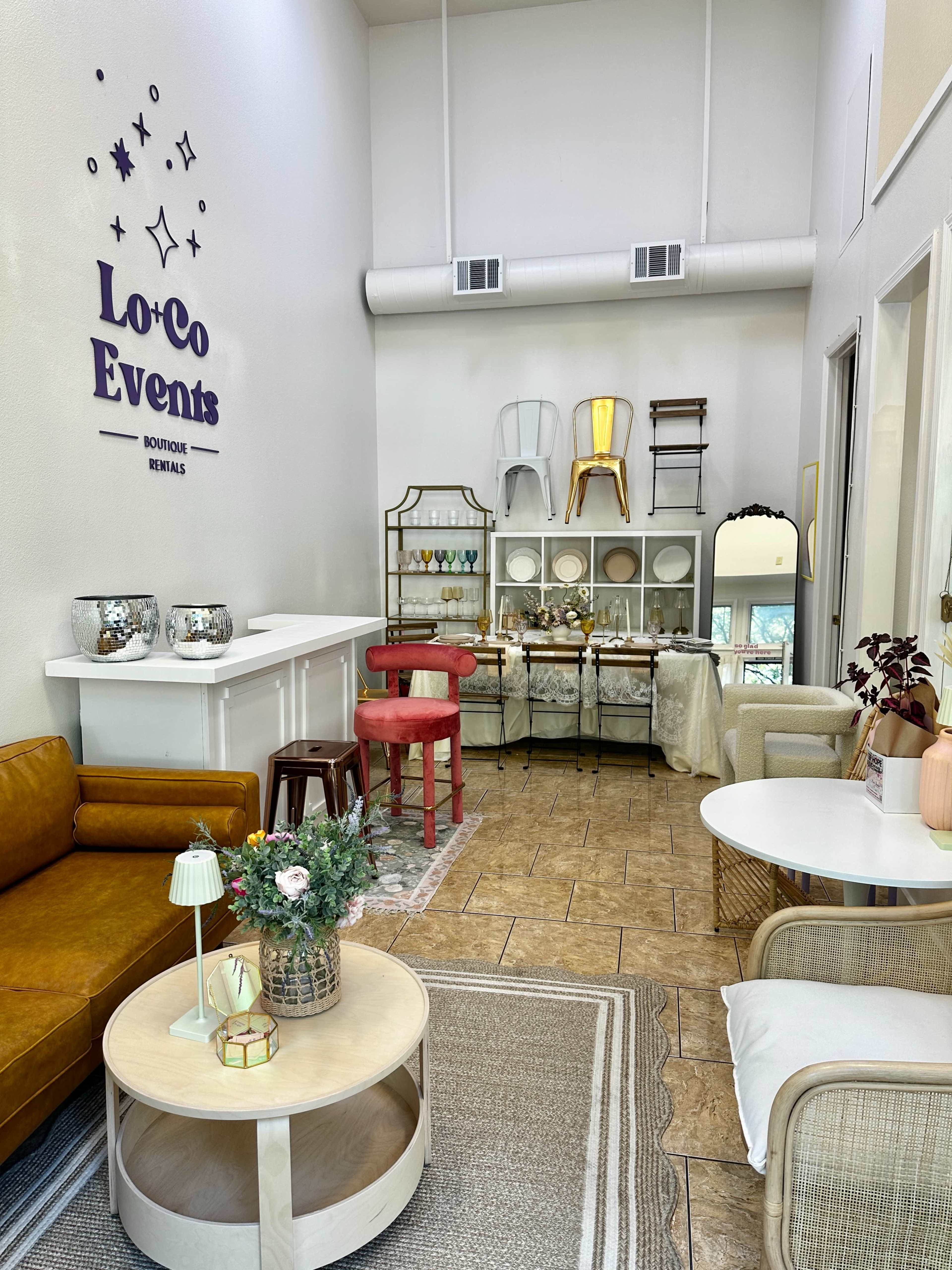 The image shows a bright, modern event rental space featuring a cozy seating area with a brown couch and various decorative items displayed on shelves.