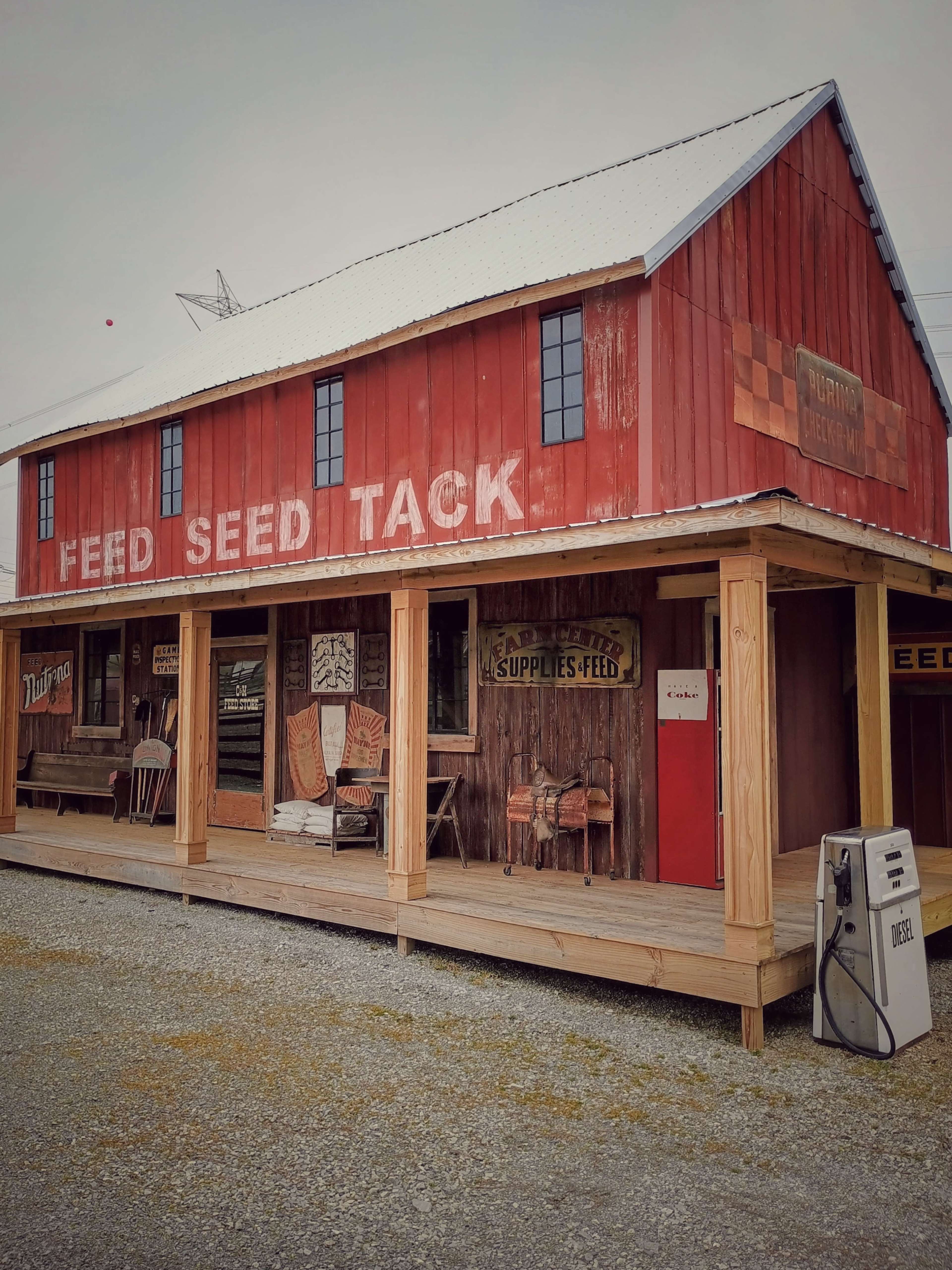 A rustic red barn features wooden decking and vintage signage, displaying "Feed," "Seed," and "Tack."