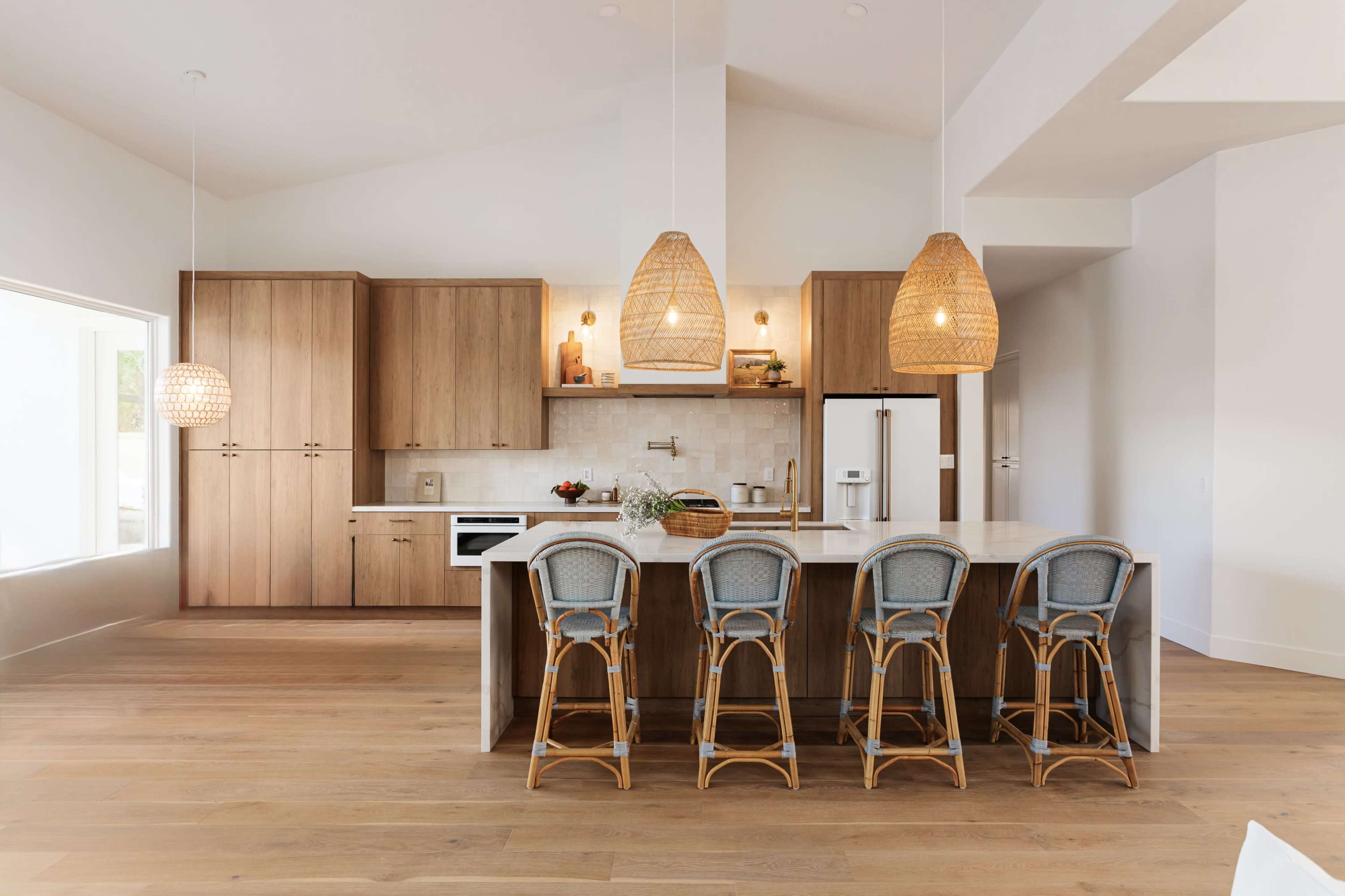 A modern kitchen features wooden cabinetry, a central island with seating, and pendant lighting.