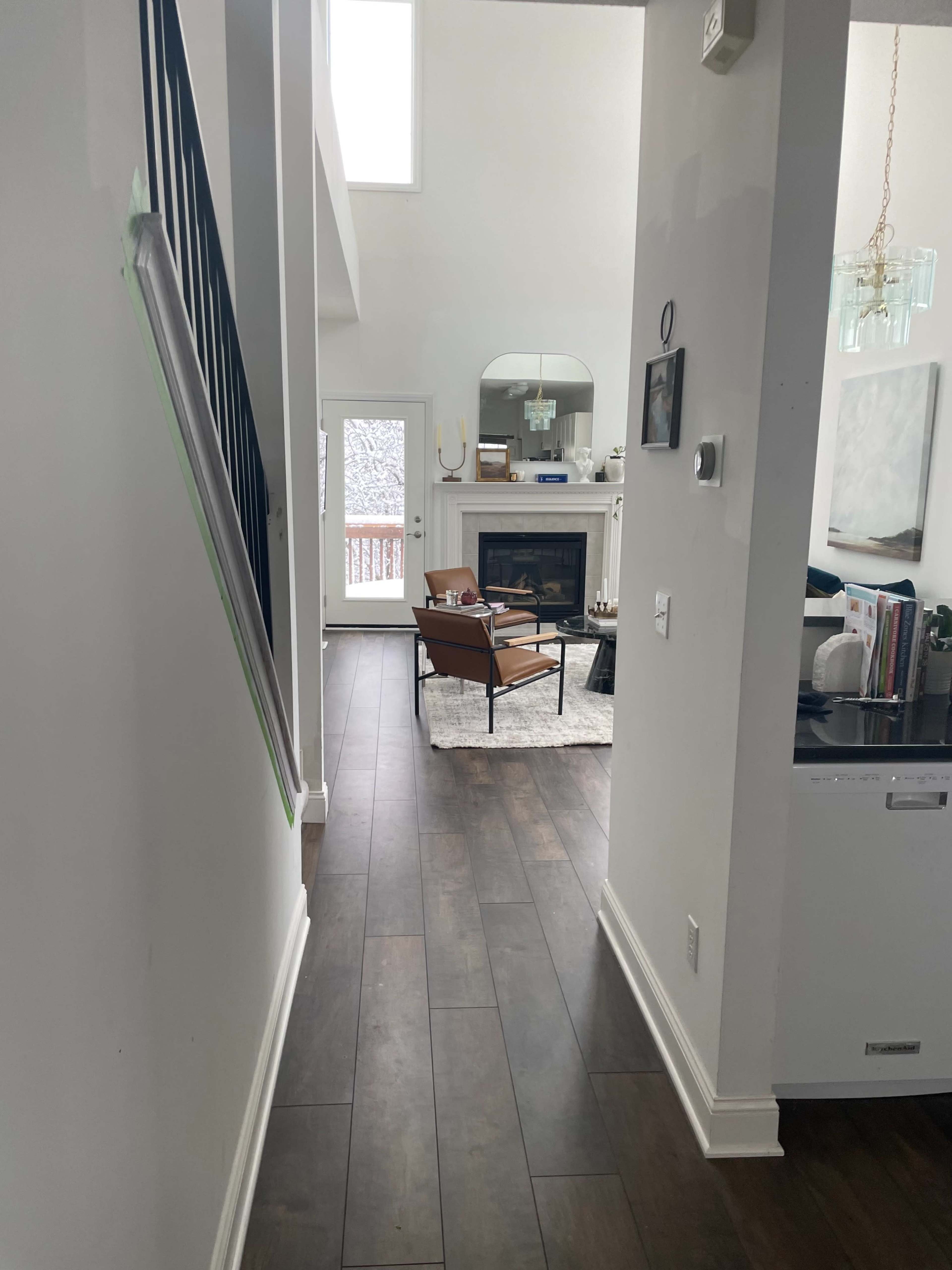 A well-lit hallway leading to a living room with a fireplace and a chair, featuring a rug on a hardwood floor.