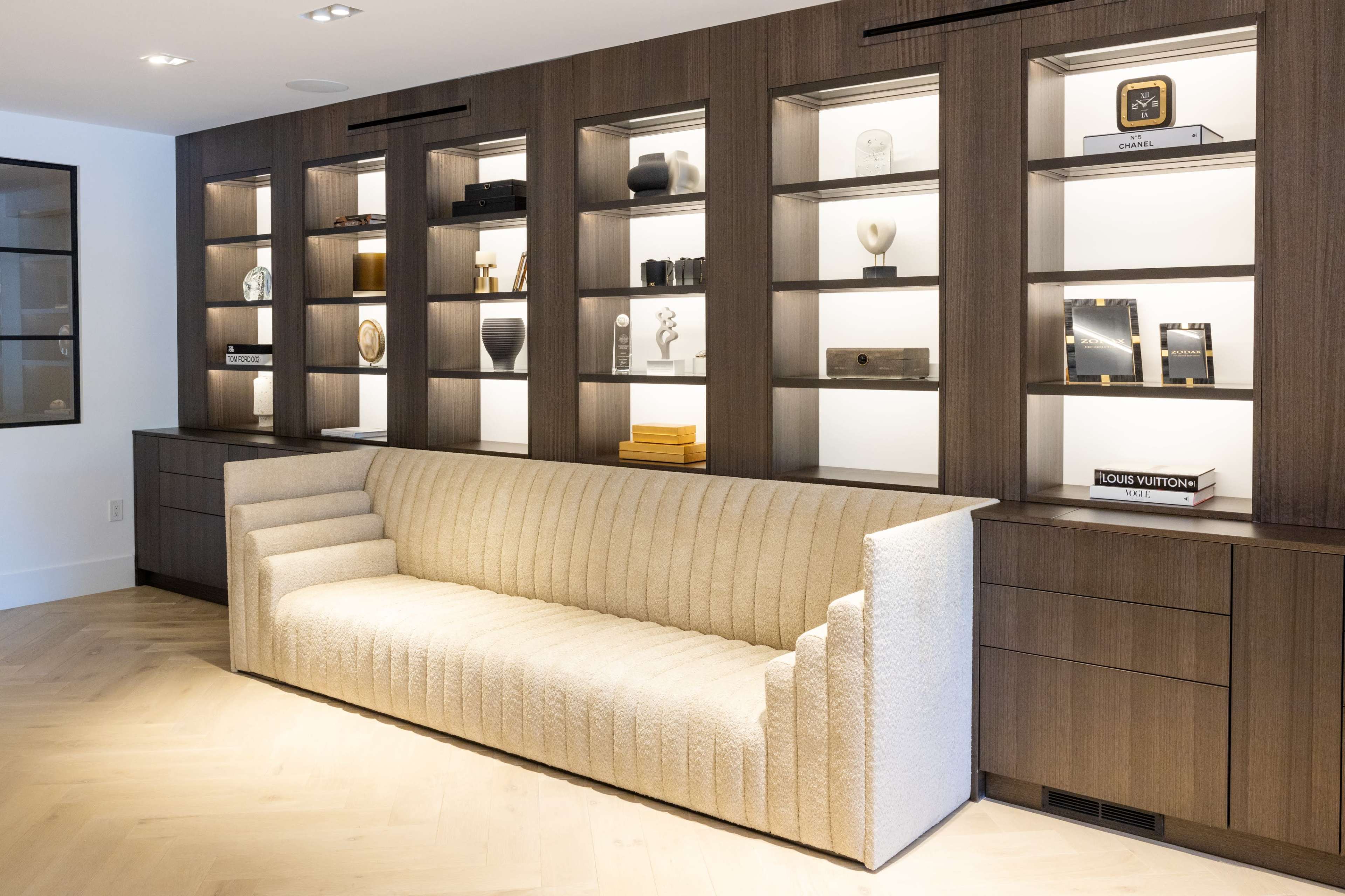 A modern living room with a textured beige sofa positioned in front of a wooden shelving unit displaying various decorative items.