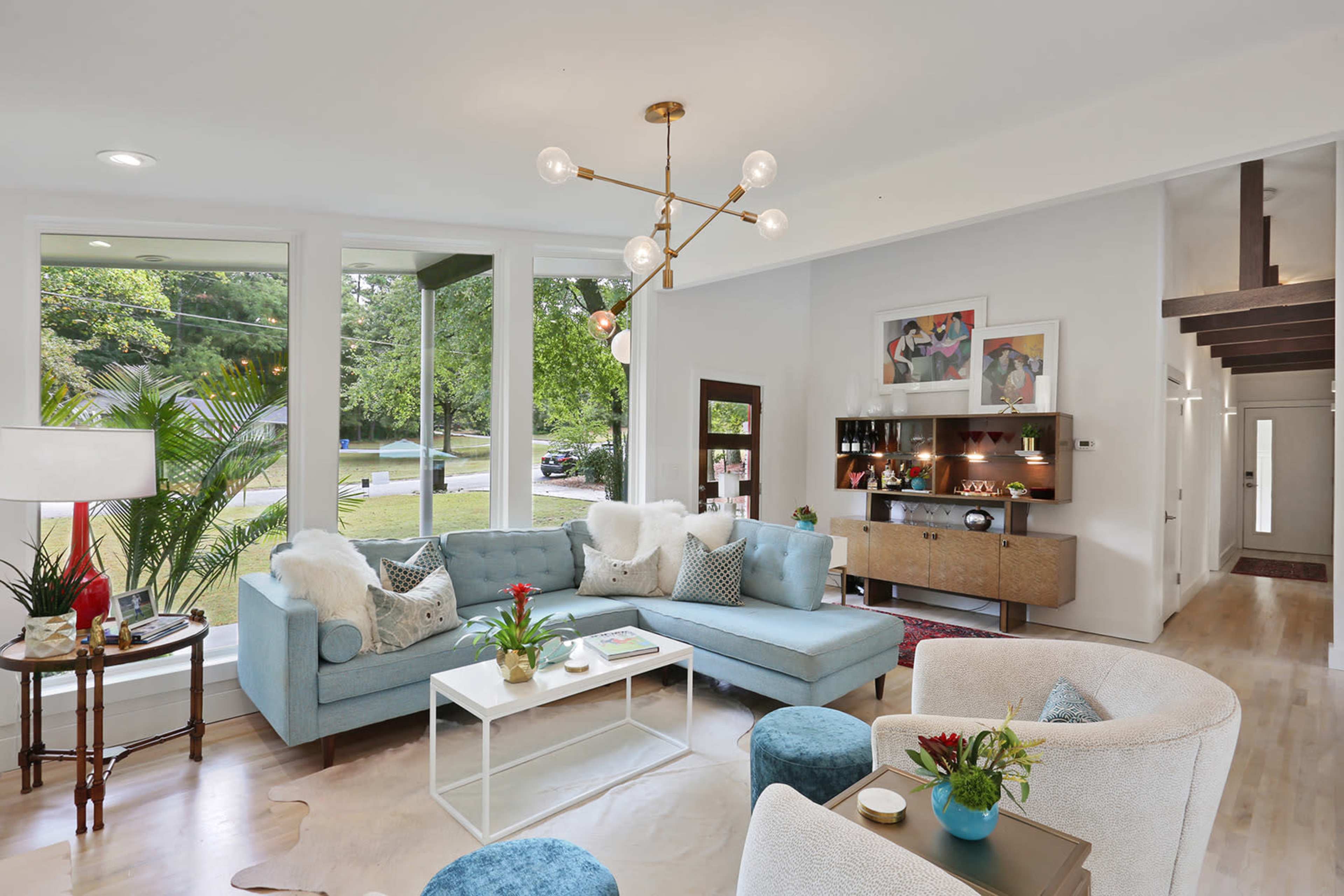 A modern living room features a light blue sectional sofa, a coffee table, and decorative elements, with large windows allowing natural light to fill the space.