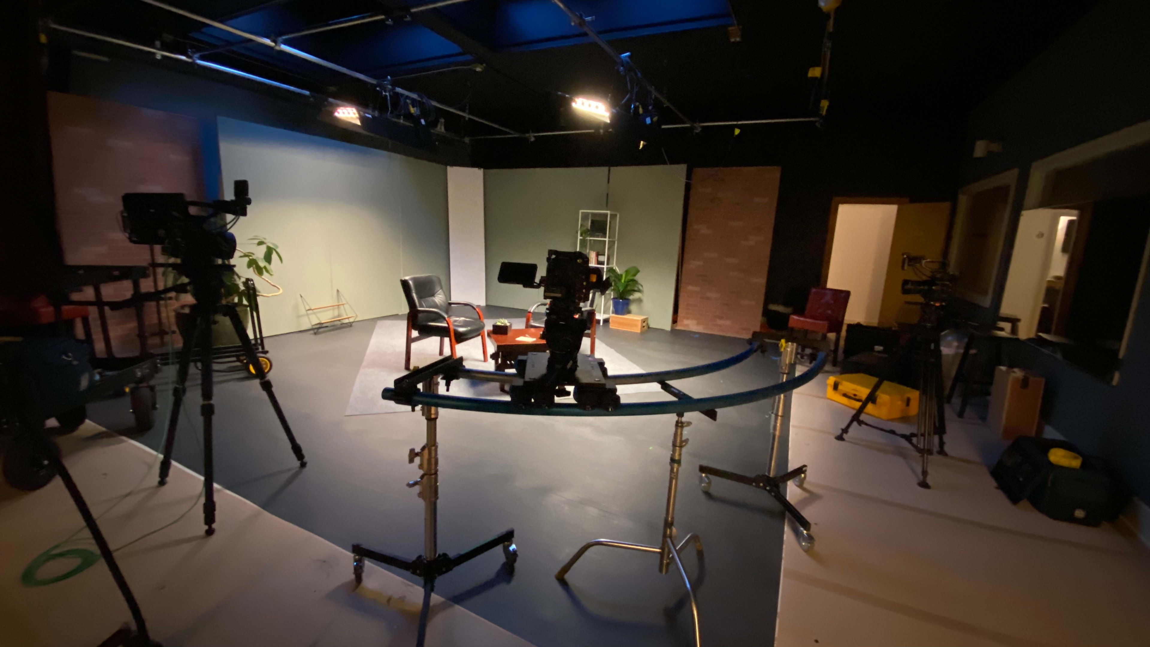 A television studio setup features multiple cameras, a circular track, two chairs, and a table in an enclosed space.