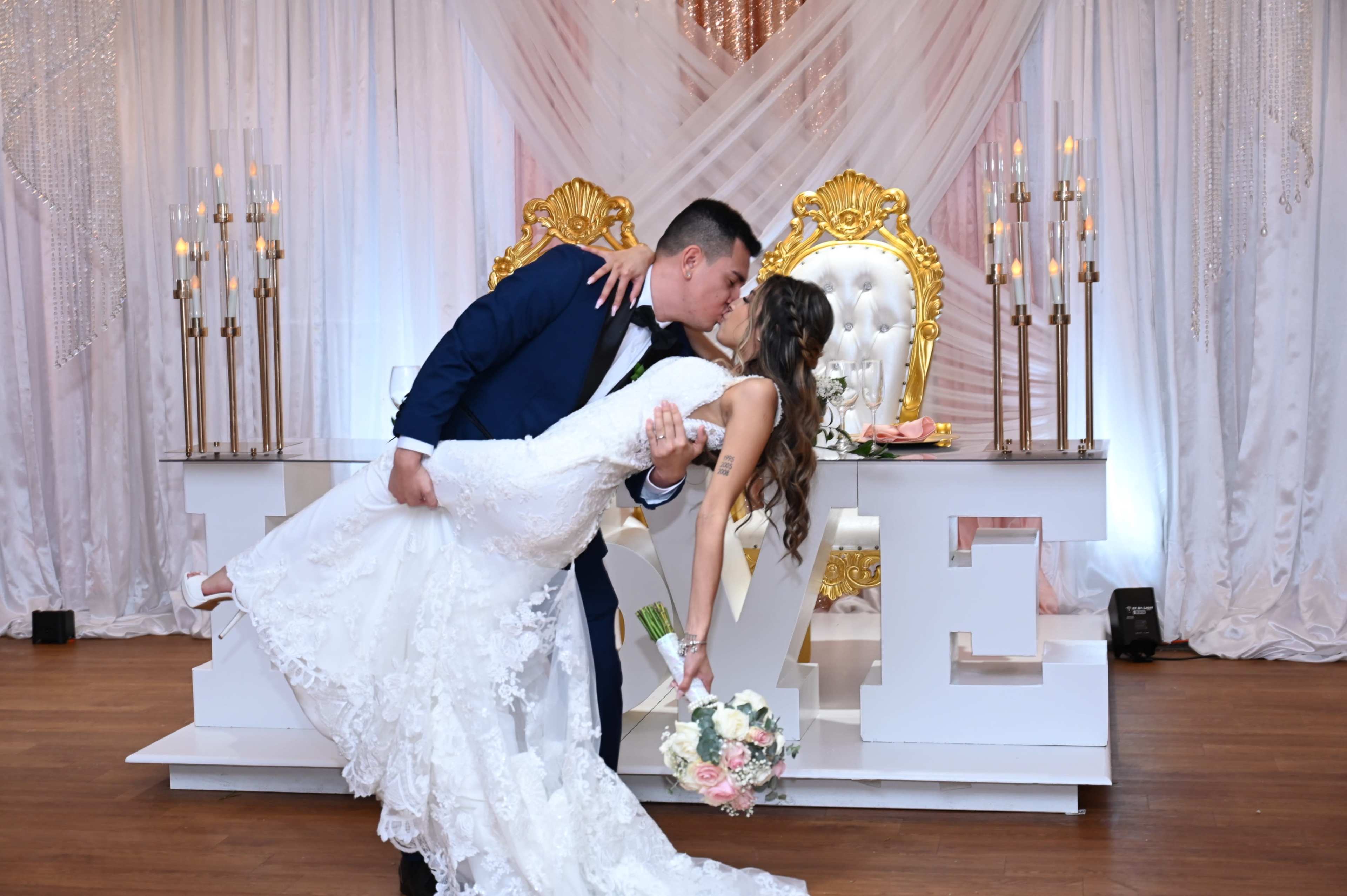 A couple shares a kiss as the groom lifts the bride in front of a decorative backdrop featuring the word "LOVE."