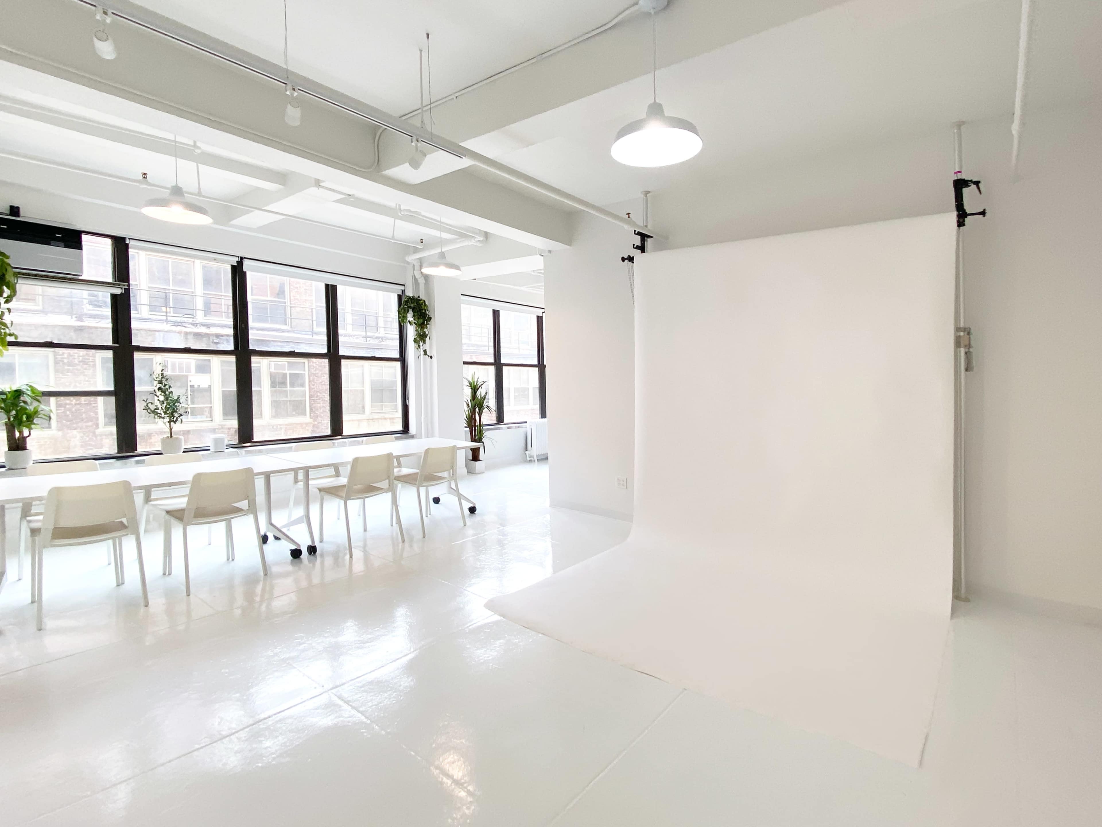 A spacious, well-lit studio with a white backdrop and a long table surrounded by chairs.