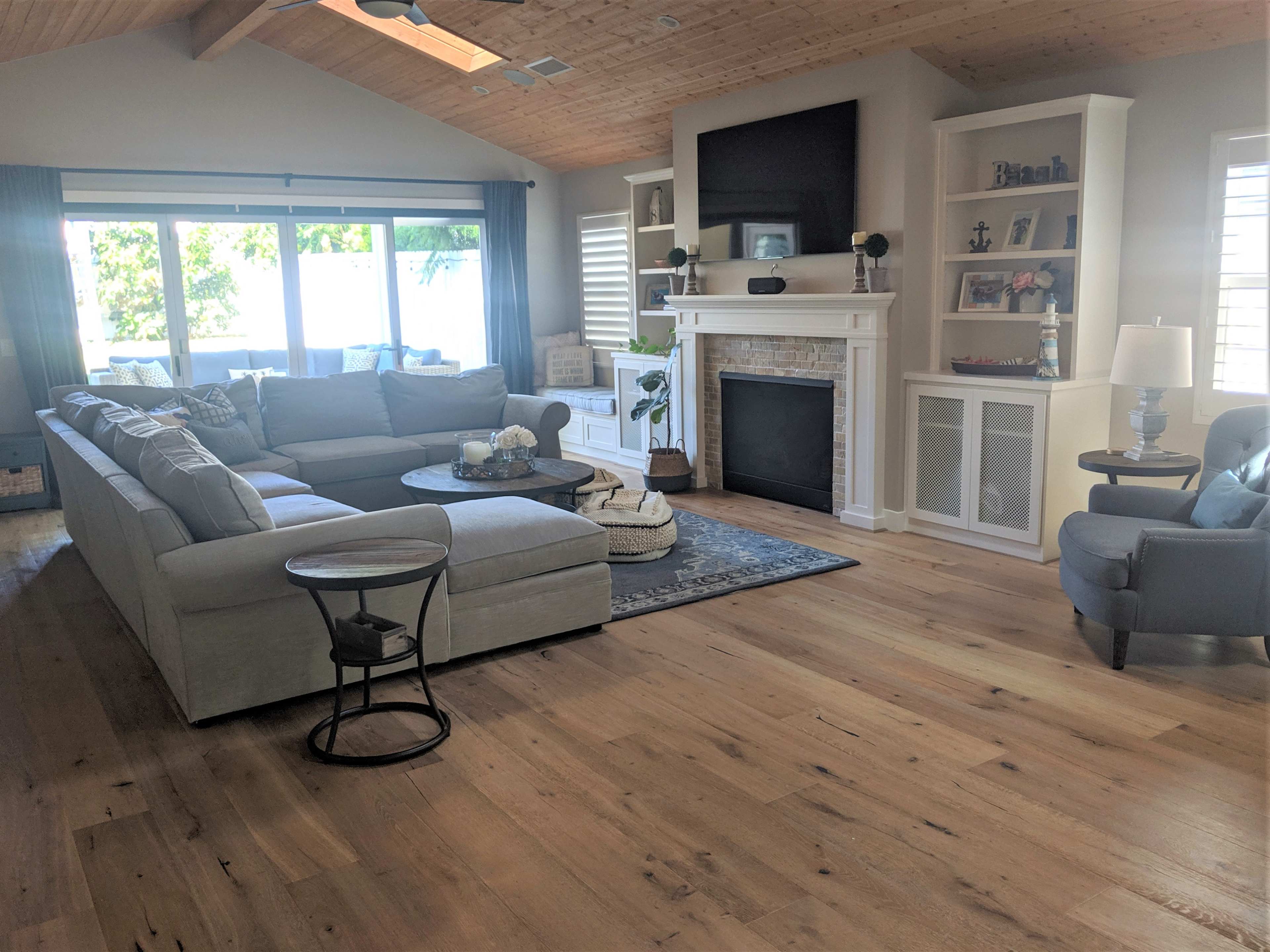 The image shows a spacious living room with a large sectional sofa, a circular coffee table, a fireplace, and windows that provide natural light.