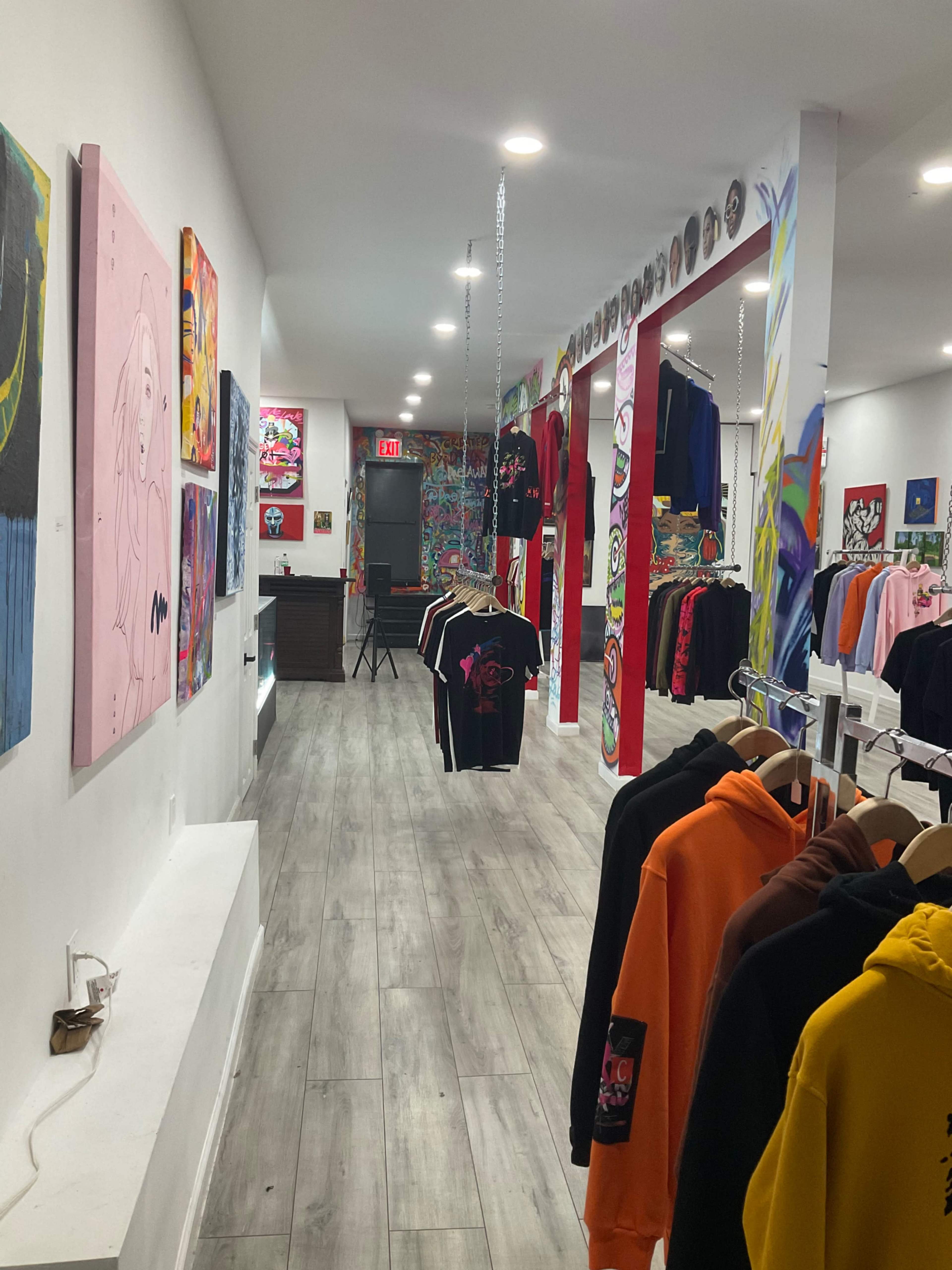 An interior view of a clothing store featuring colorful streetwear hanging on racks, with vibrant artwork displayed on the walls.