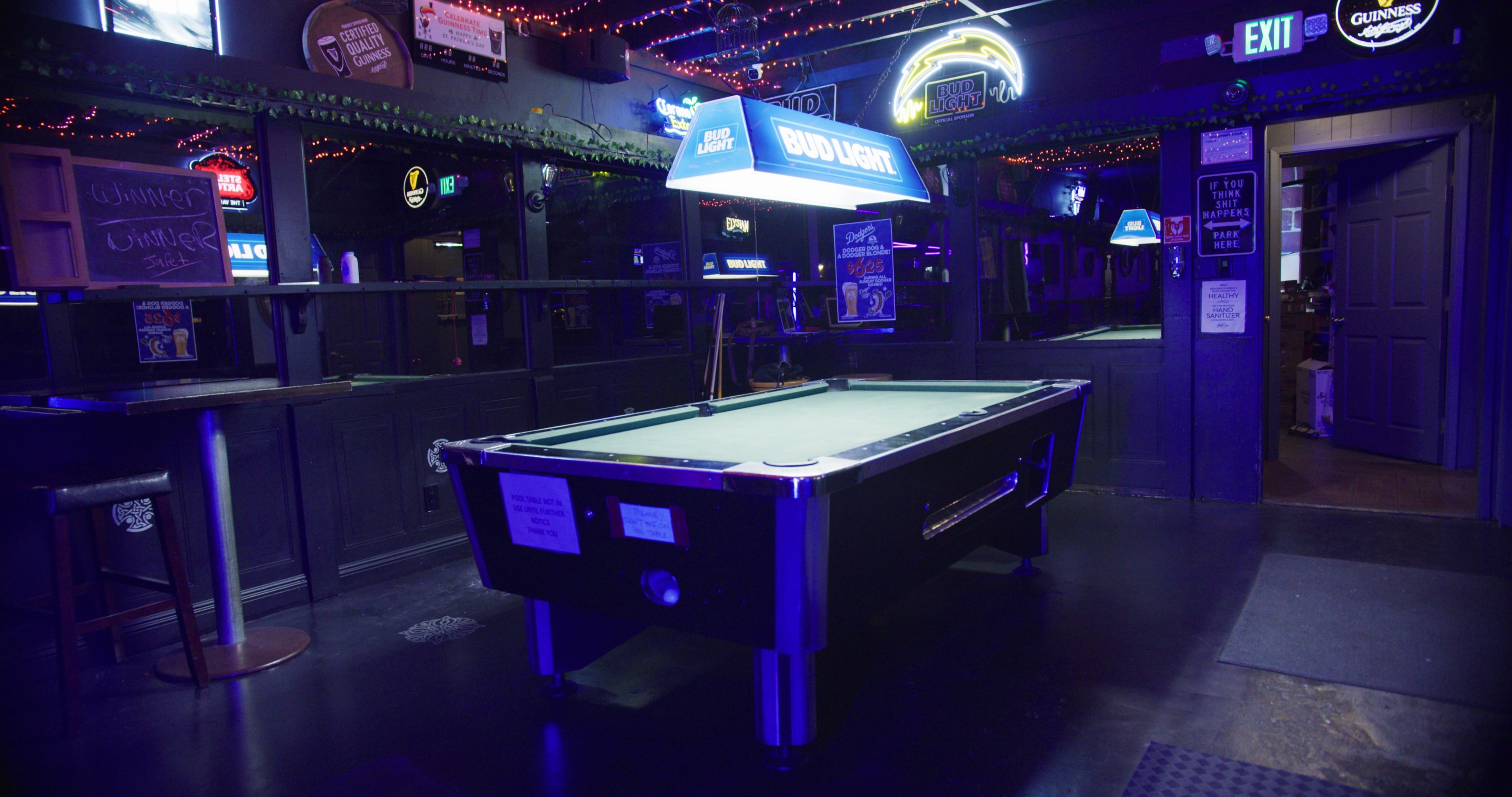 An empty pool table under a illuminated Bud Light sign in a dimly lit bar.