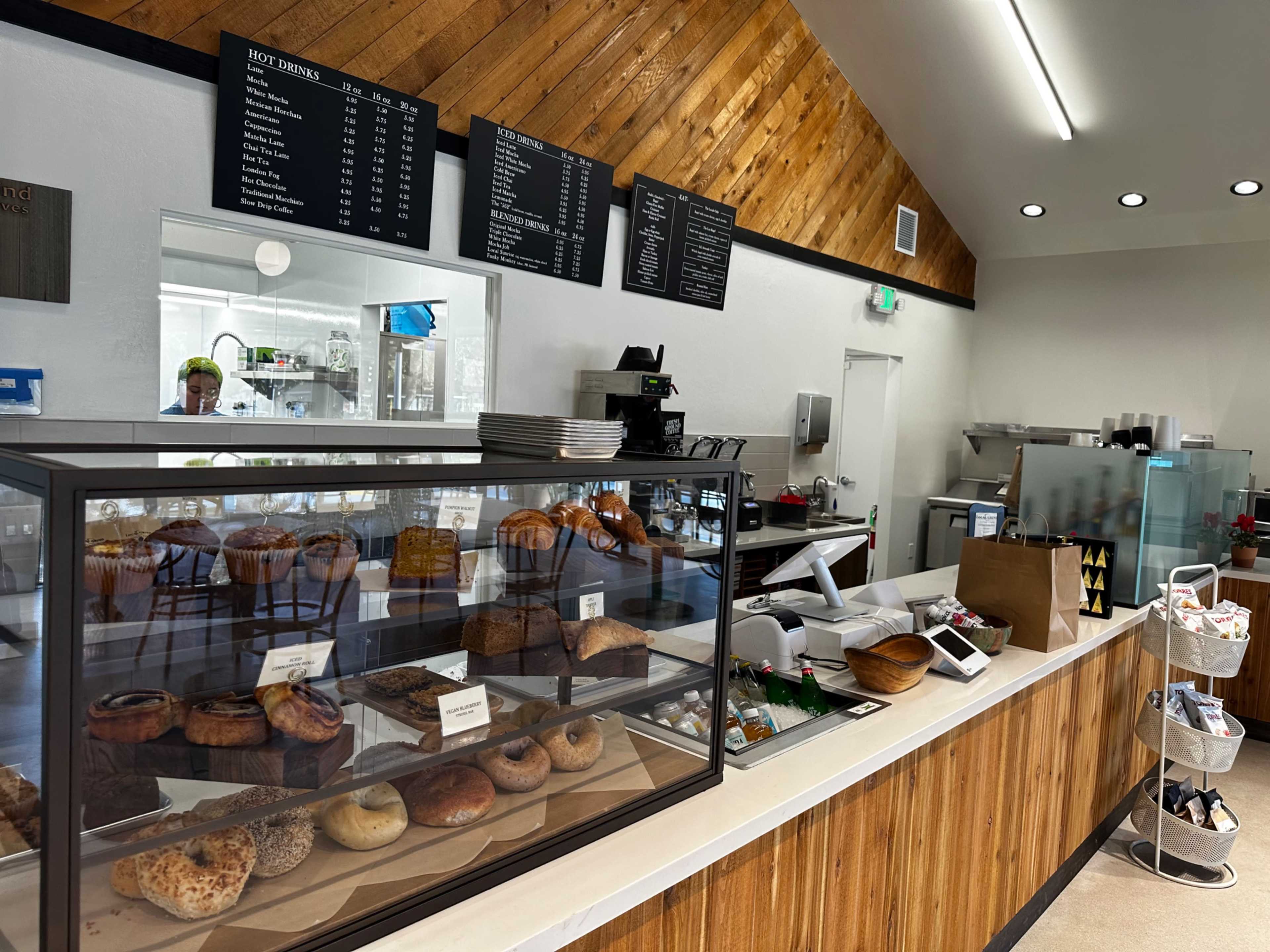 A bakery counter displaying an assortment of baked goods, with a menu board and a barista behind the counter.
