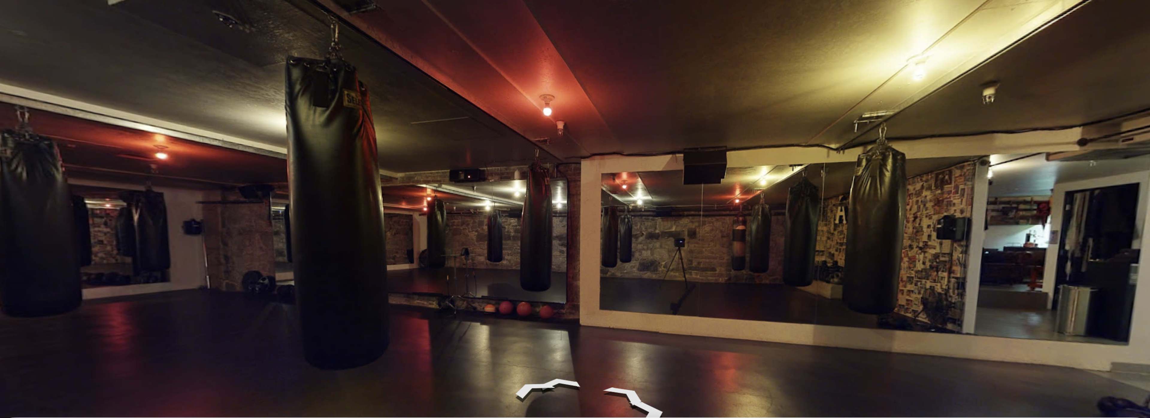 A boxing training gym with several hanging punching bags and mirrors on the walls.