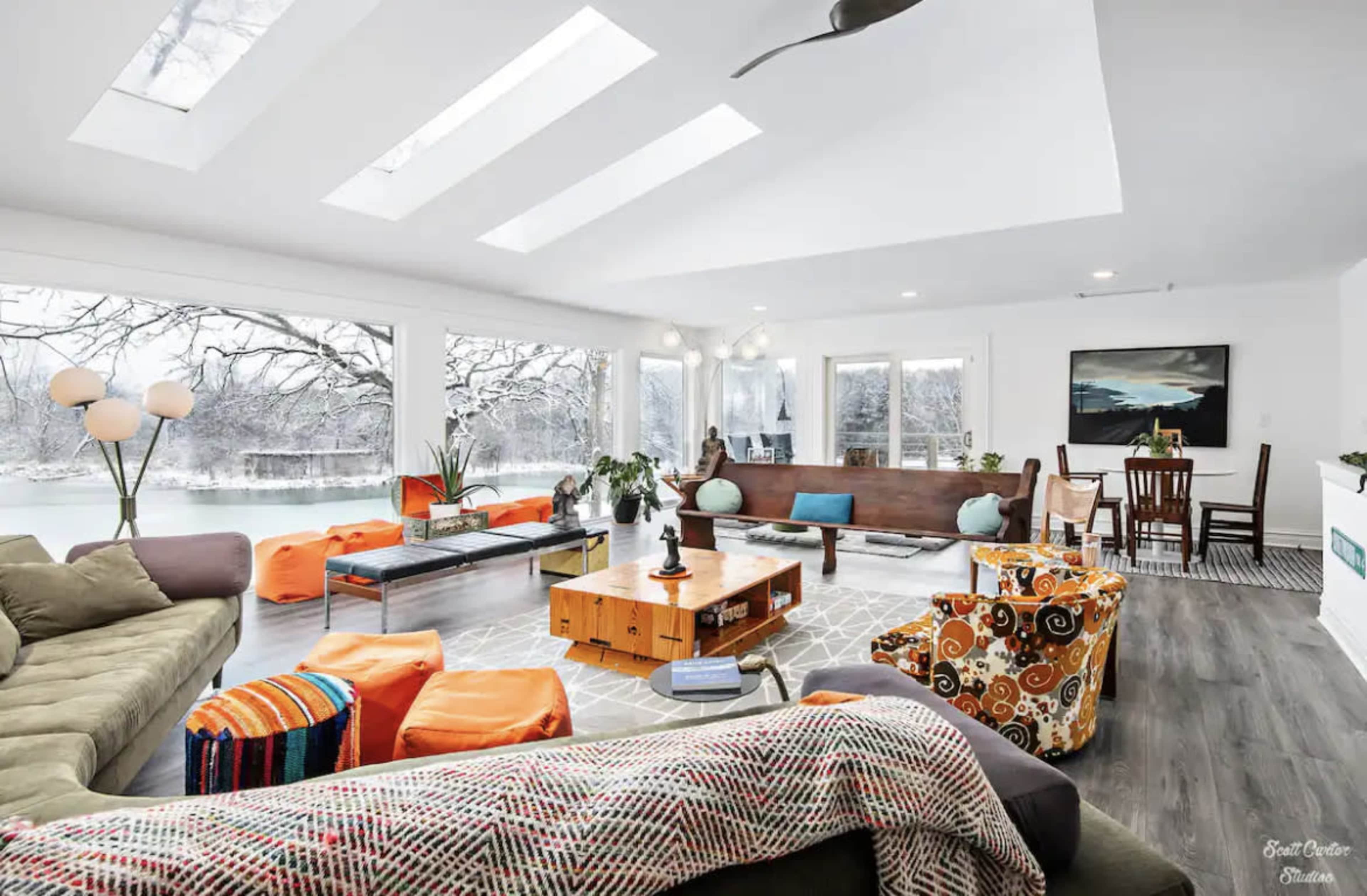 The spacious living room features large windows overlooking a snowy landscape, with comfortable seating, a coffee table, and a dining area.