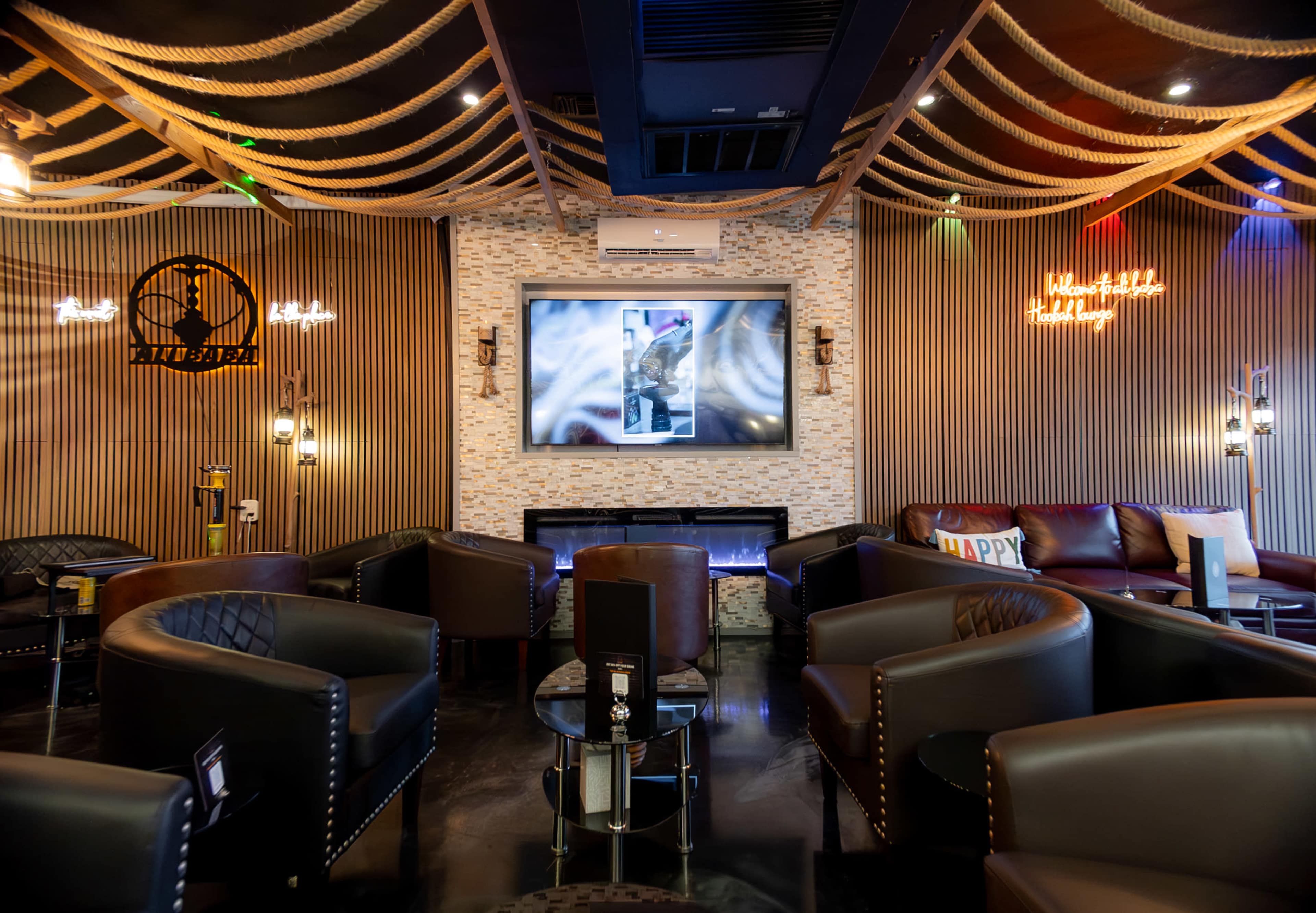 A lounge area with dark leather seating, a large wall-mounted screen, and decorative lighting along the ceiling.