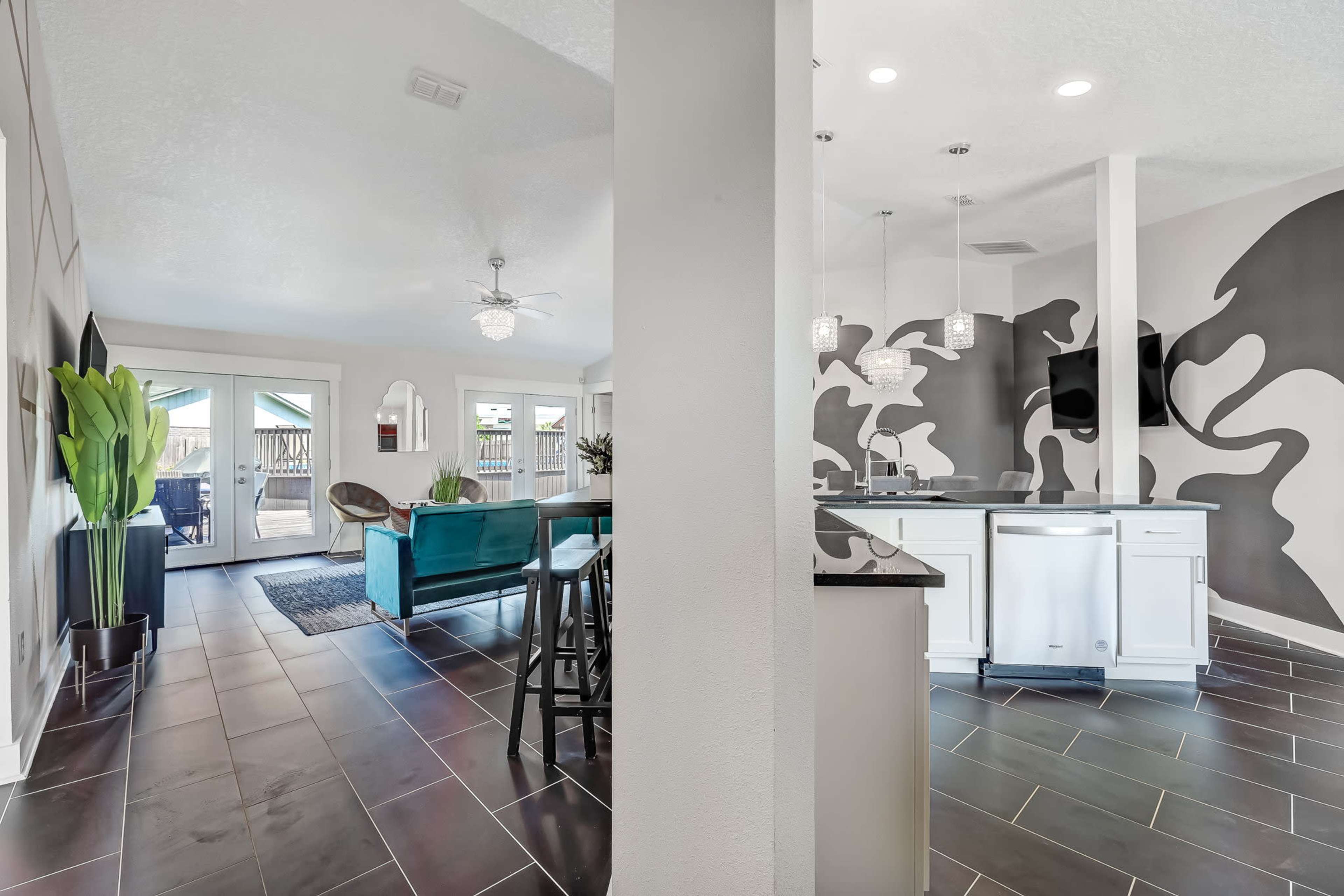 An open-concept living area with a kitchen featuring a modern design, contrasting black and white walls, and seating areas leading to an outdoor patio.