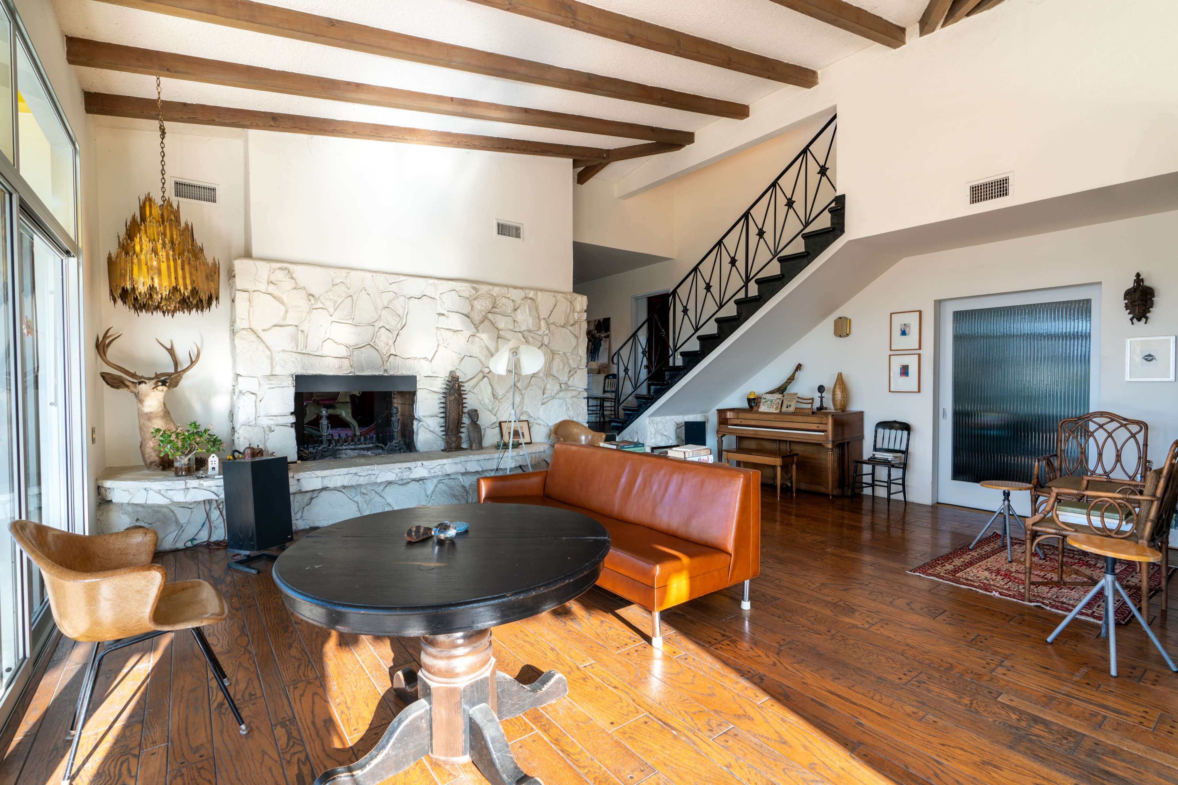 A spacious living room with a stone fireplace, wooden beams on the ceiling, and a mix of modern and rustic furniture.